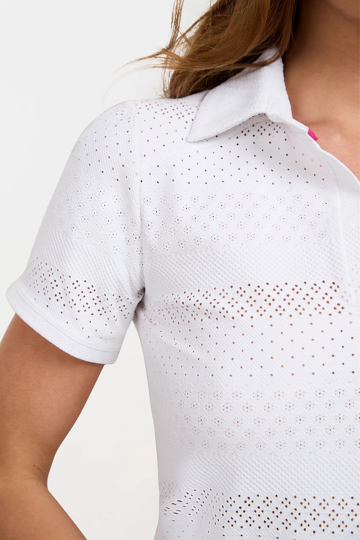 A close-up of a person wearing the Lace Polo—a white, short-sleeved collared shirt with small laser-cut perforations. The person's hair is partially visible.