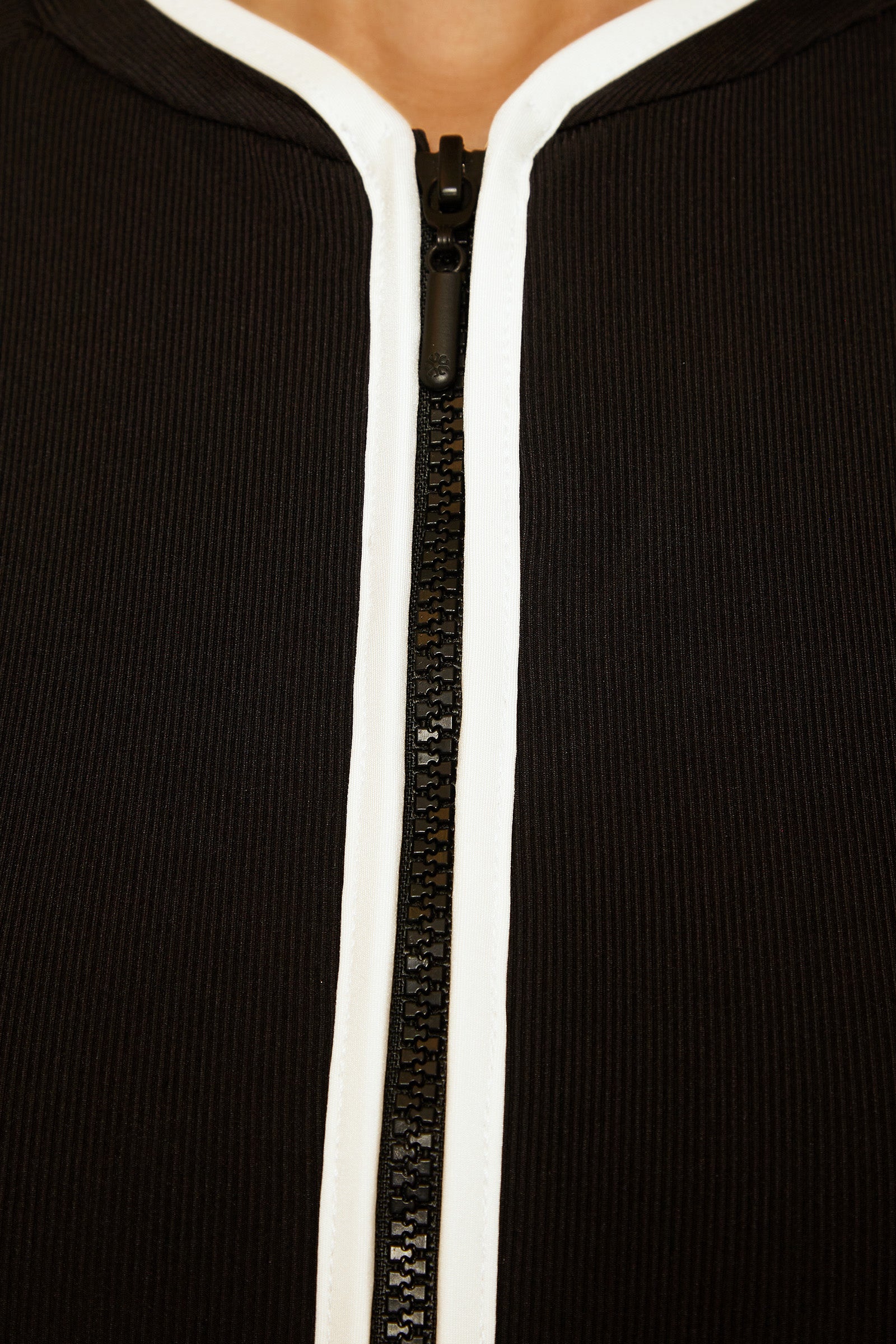 Close-up of the Triumph Short-Sleeve Zip-Up Paddlesuit in black, featuring ribbed fabric and a central black zipper with white trim, partially unzipped at the neckline to reveal a hint of skin.