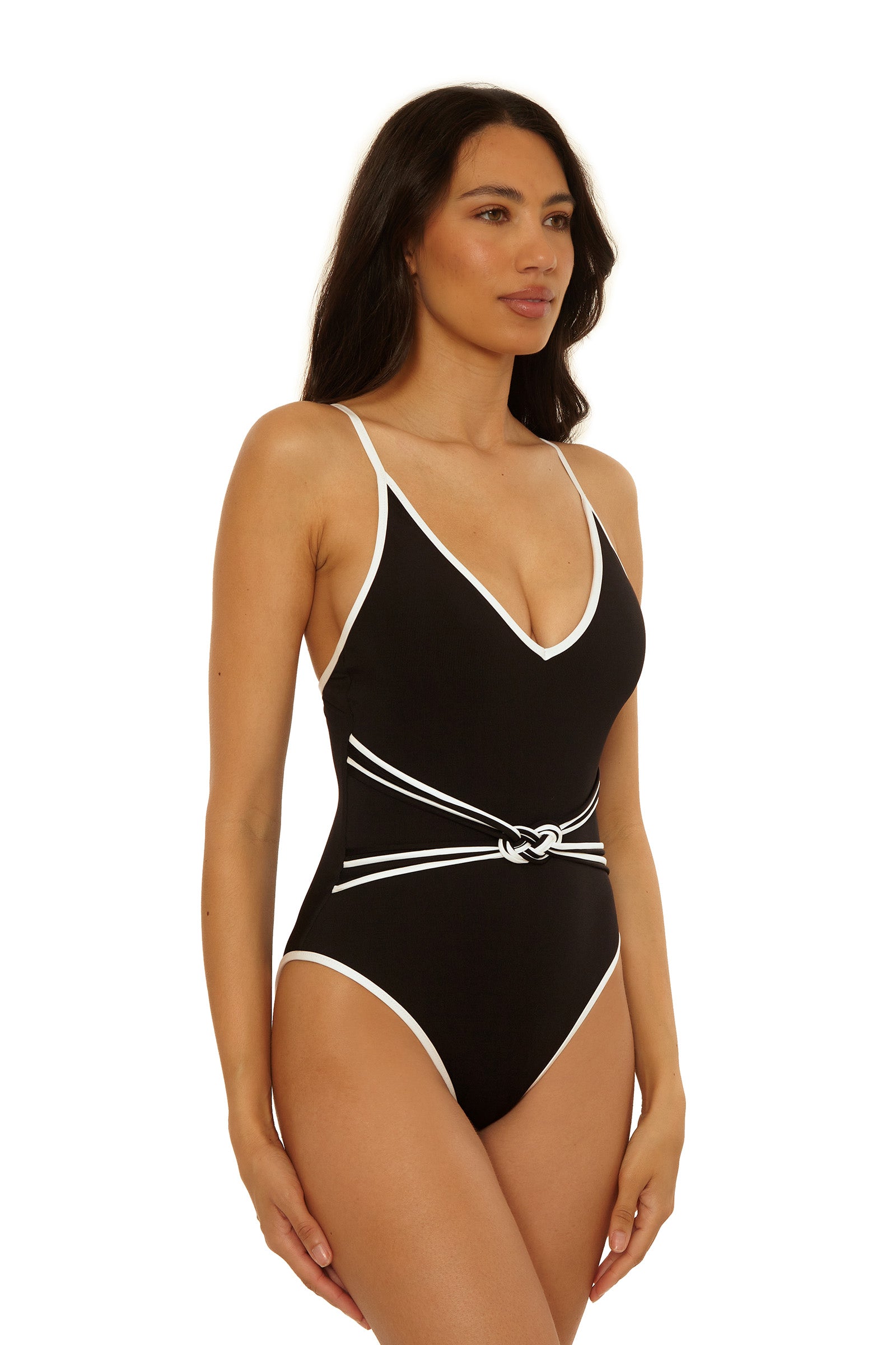 A woman models the Triumph Braided One-Piece Swimsuit, featuring black fabric with white trim and a knotted white belt, set against a plain white background.