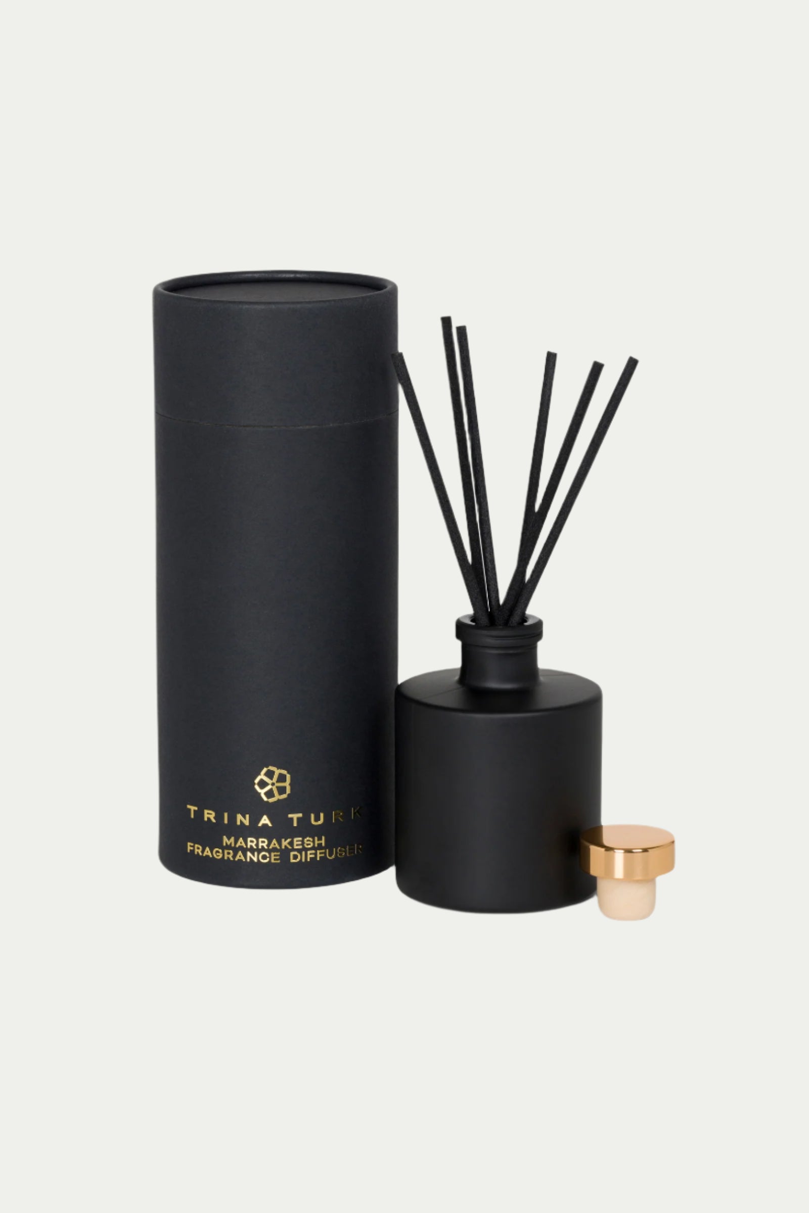 The TT x Perch Marrakesh Fragrance Diffuser features a sleek black design with matching reeds, a cylindrical container, and a small gold cap, all showcasing luxurious gold text against a plain light background.