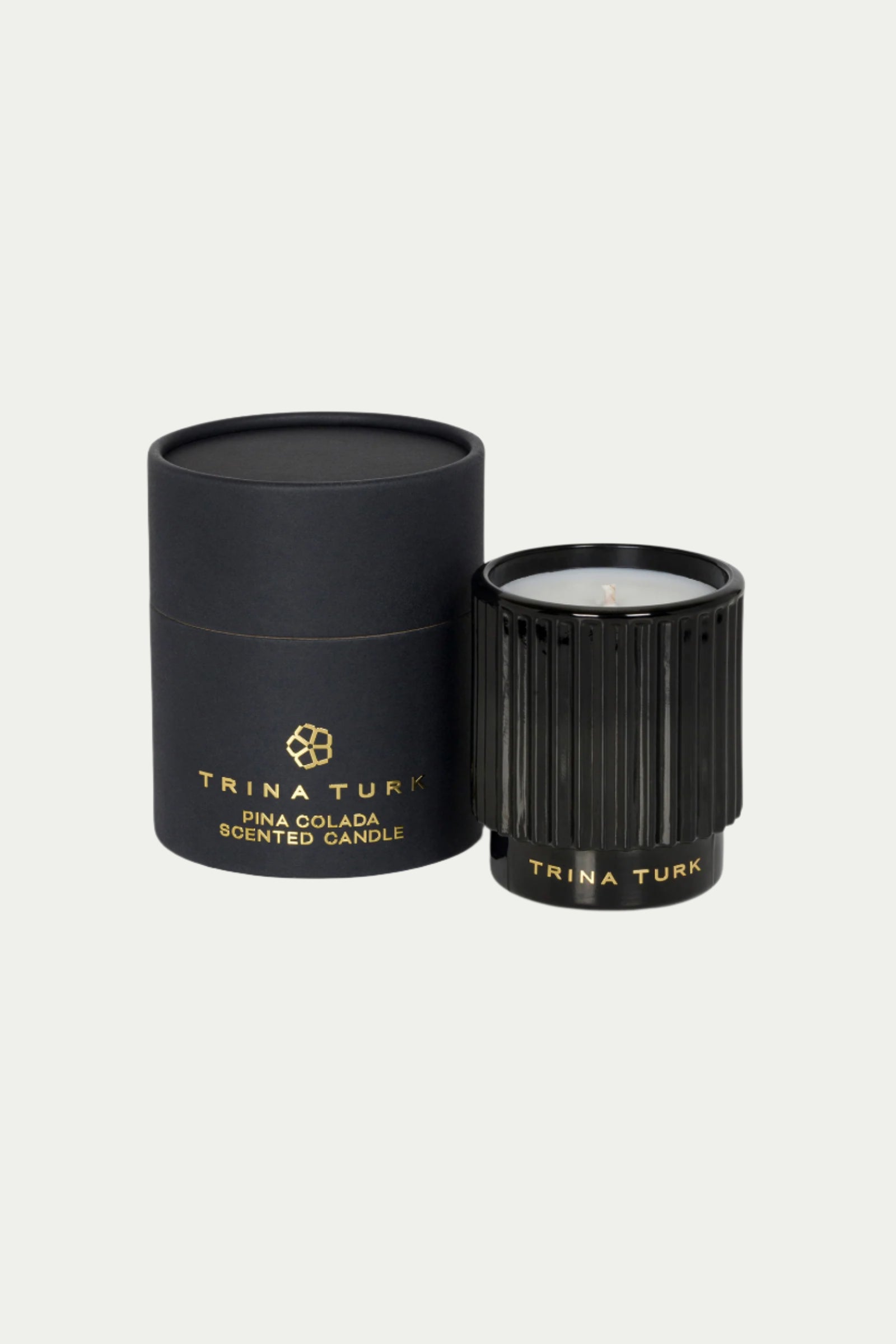 A black TT x Perch Pina Colada Candle with gold lettering is displayed next to its matching black and gold cylindrical box on a light background.