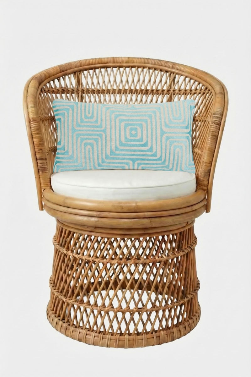 A round wicker chair with a cream cushion and the Amazing Maze Embroidered Lumbar Pillow, which is rectangular, light blue, and features a geometric pattern, set against a plain white background.