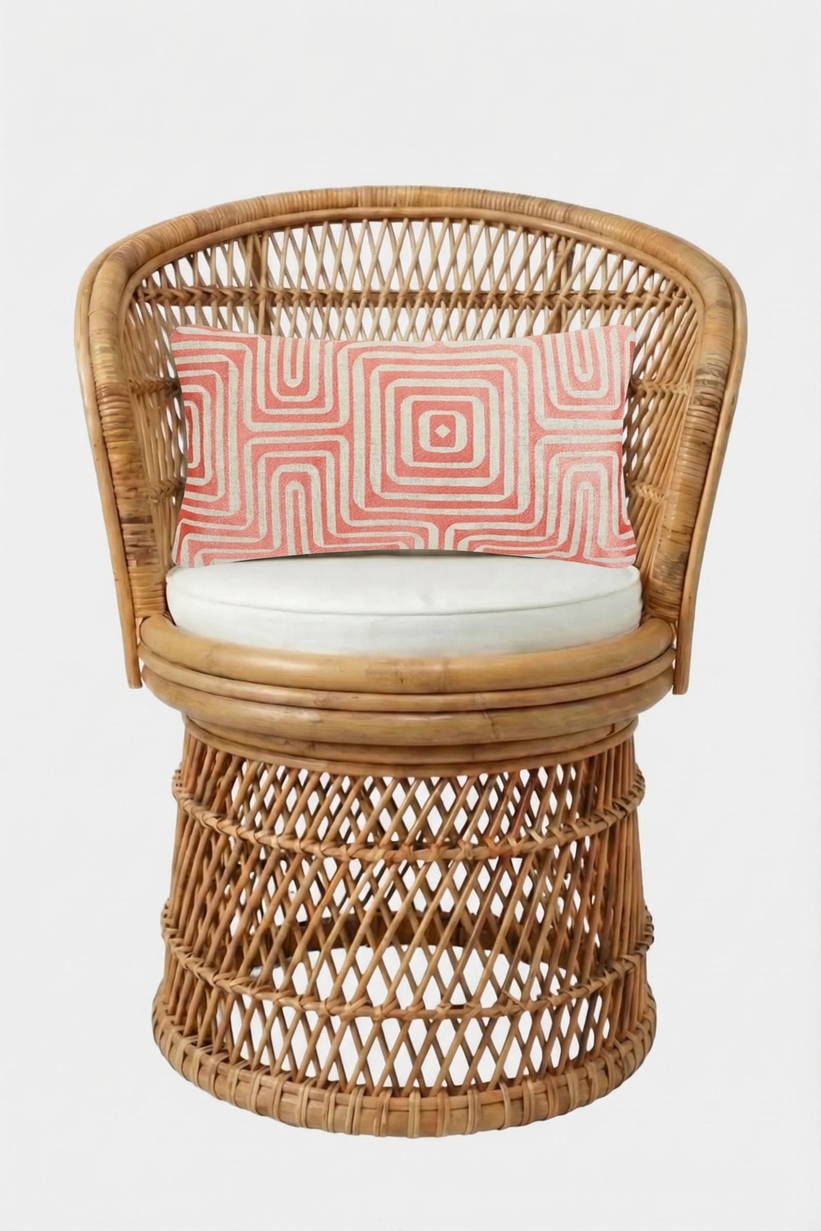 A round rattan chair with a cream cushion and the Amazing Maze Embroidered Pillow, which has a red and white geometric design, set against a plain white background.