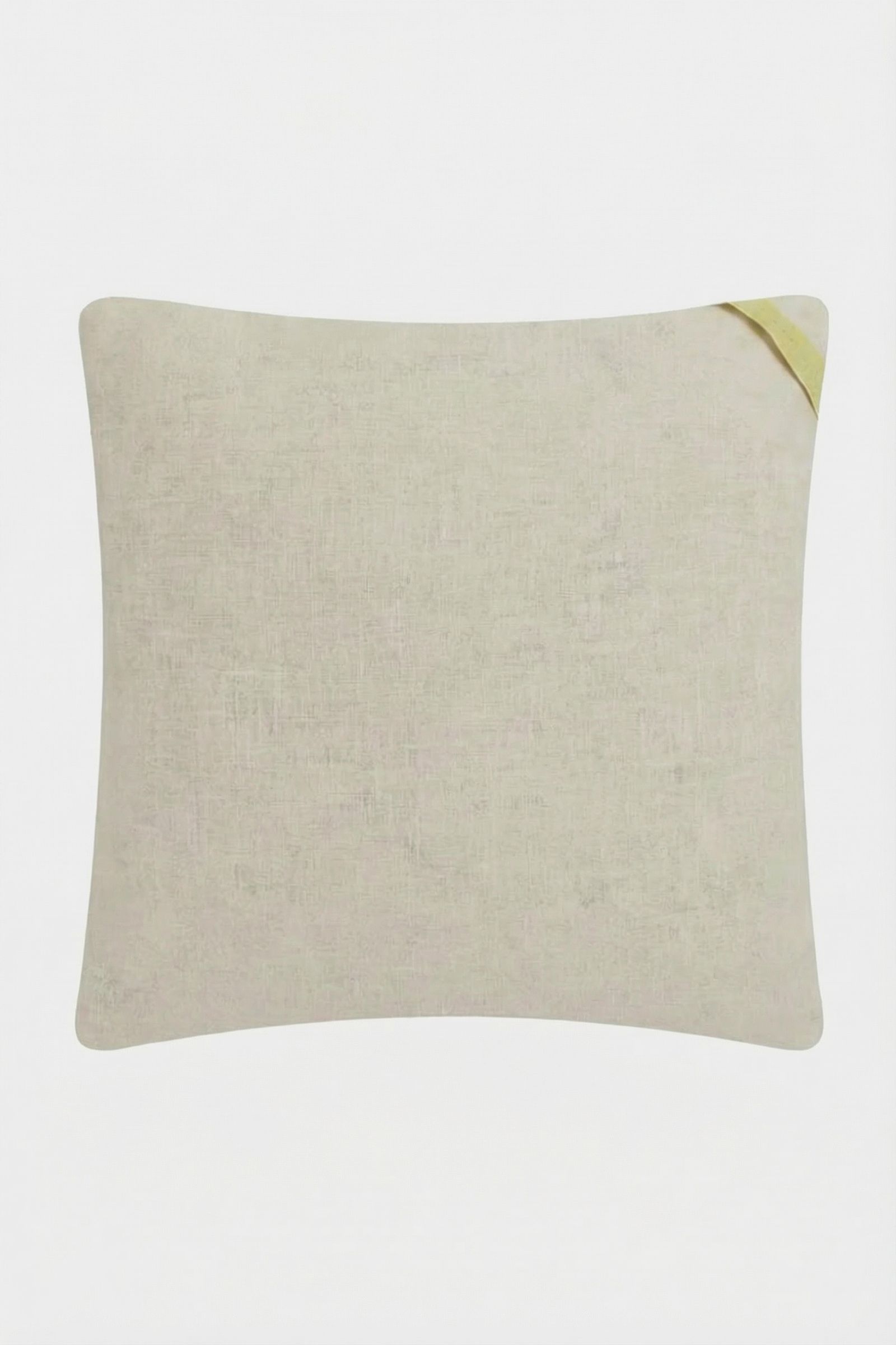 The Costa Mesa Embroidered Square Pillow is a light beige, rectangular cushion with a subtle textured pattern and a small diagonal yellow fabric loop at one corner, shown on a plain white background.