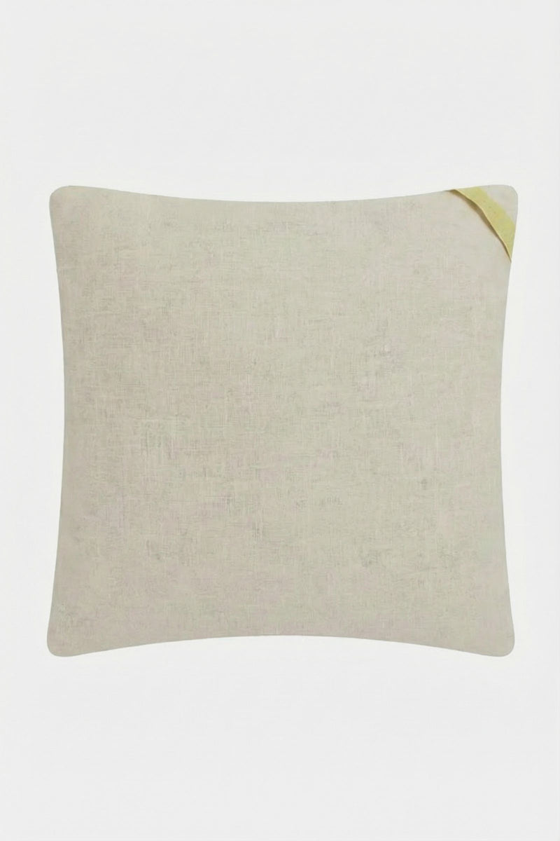 The Ogee Amber Embroidered Square Pillow features a subtle textured beige fabric with a small diagonal strap in the top right corner, displayed against a white background.