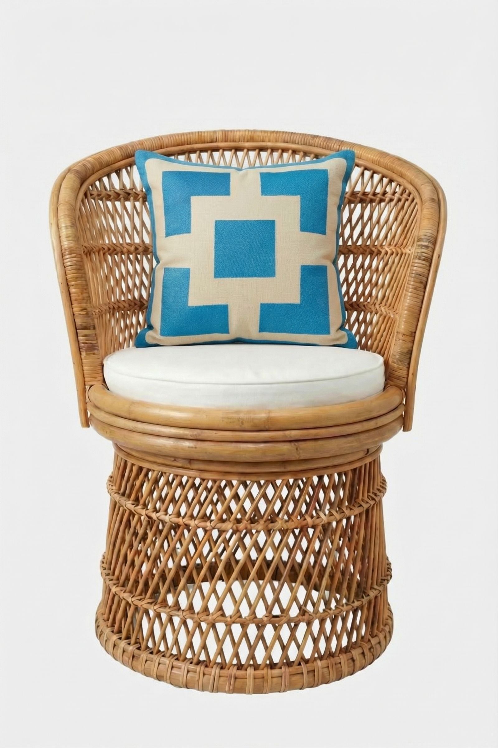 A wicker chair with a round white cushion and the Palm Springs Block Embroidered Pillow—blue, 20"x20", bold geometric pattern, soft cover—set against a plain white background.