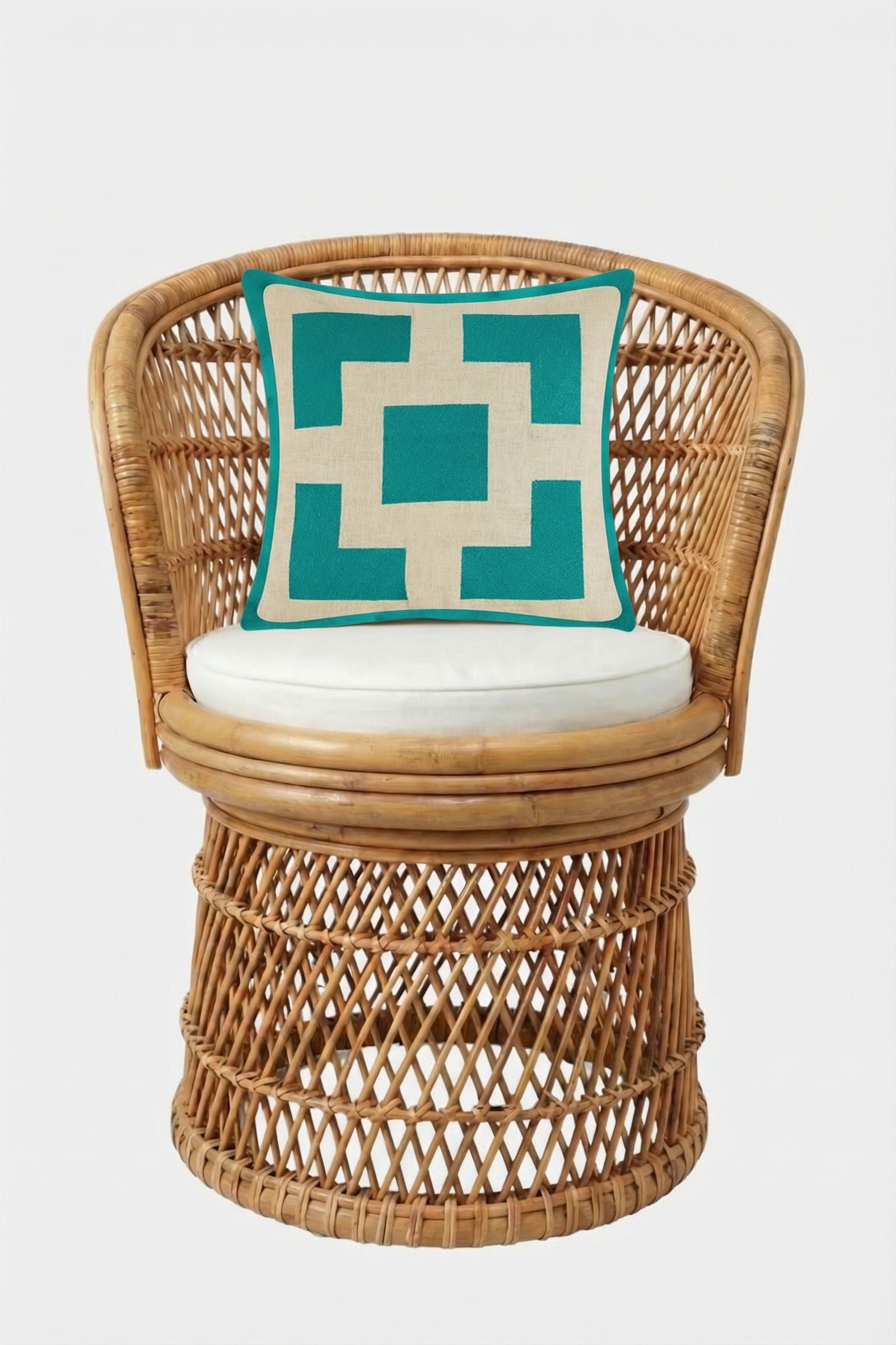 A round wicker chair with a white cushion, featuring the Palm Springs Block Embroidered Pillow (20"x20") with a geometric turquoise and white pattern, set against a plain white background.