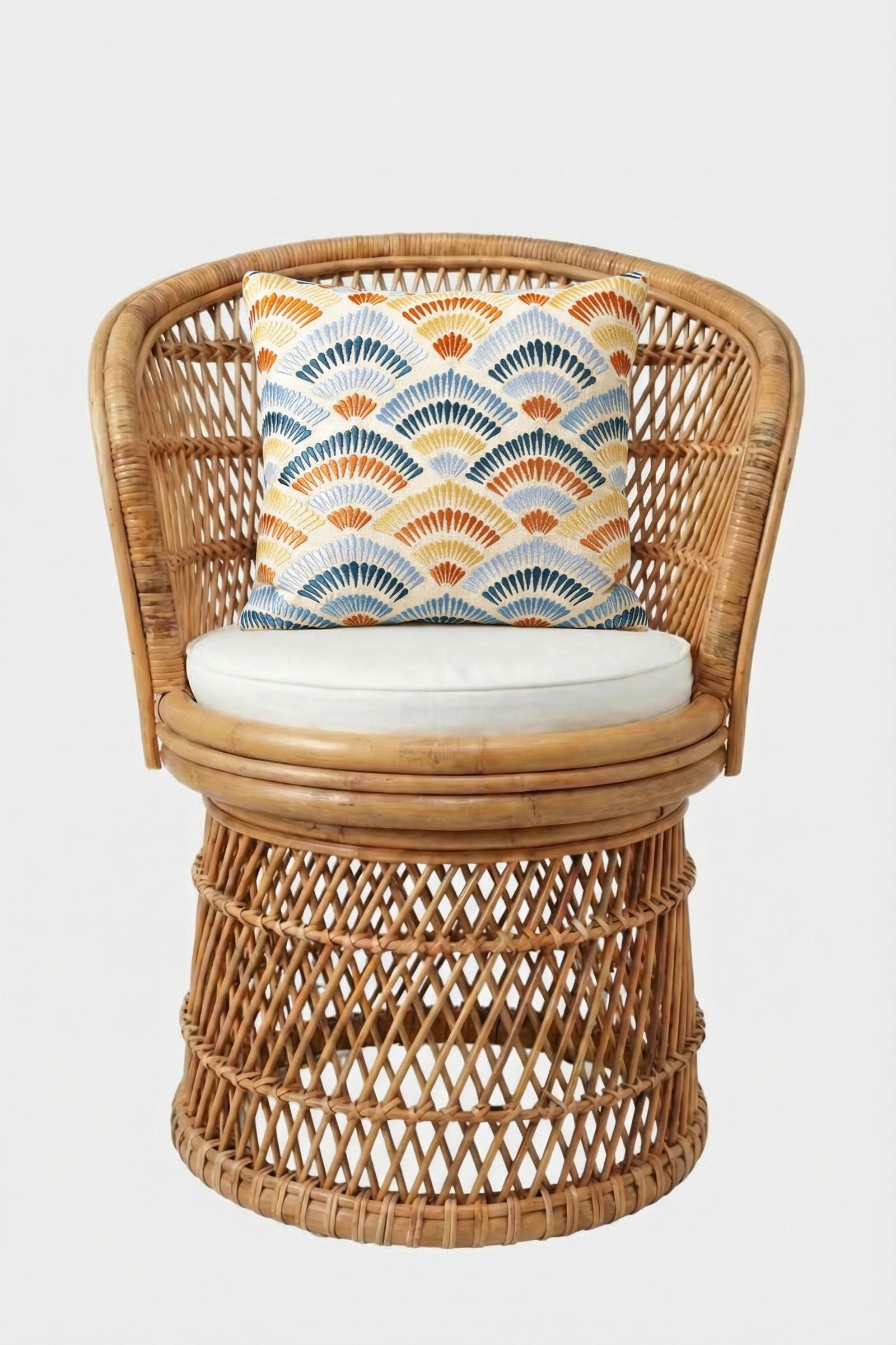 A round rattan chair with a white seat cushion and the Pasadena Embroidered Throw Pillow, which has an orange, blue, and yellow fan pattern, set against a plain white background.