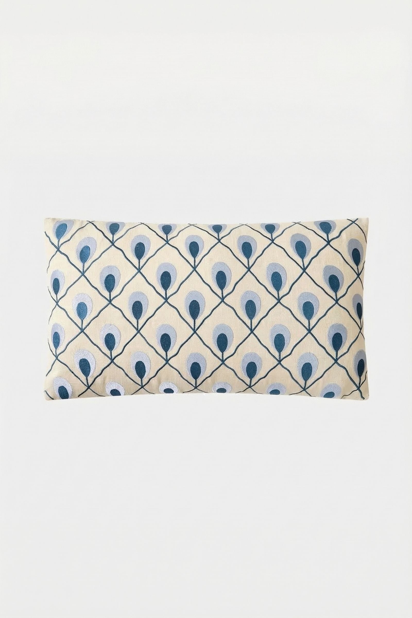 The Roseville Embroidered Lumbar Pillow is a rectangular, cream pillow featuring a repeating blue and teal peacock feather design on a white background.