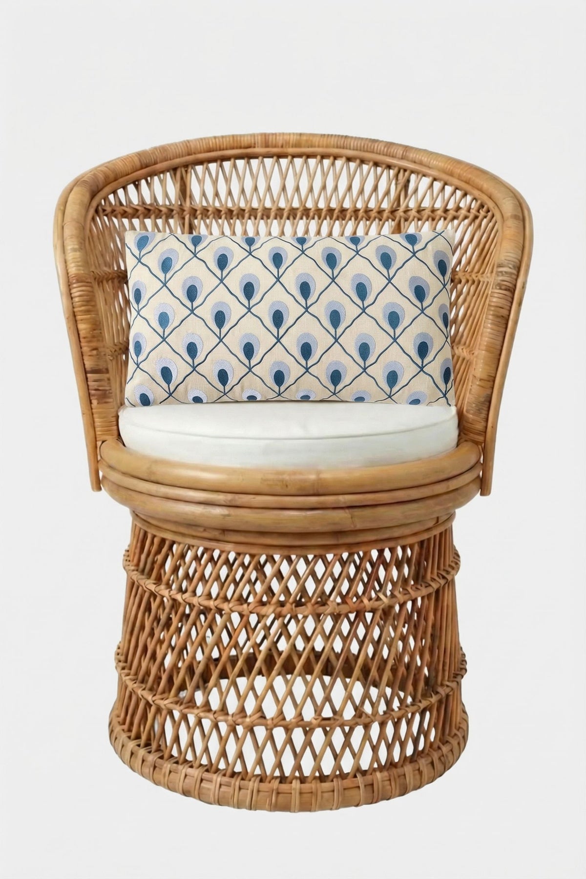 A round rattan chair with a woven design, featuring a white seat cushion and the Roseville Embroidered Lumbar Pillow, which showcases a blue and white peacock feather pattern, set against a plain white background.