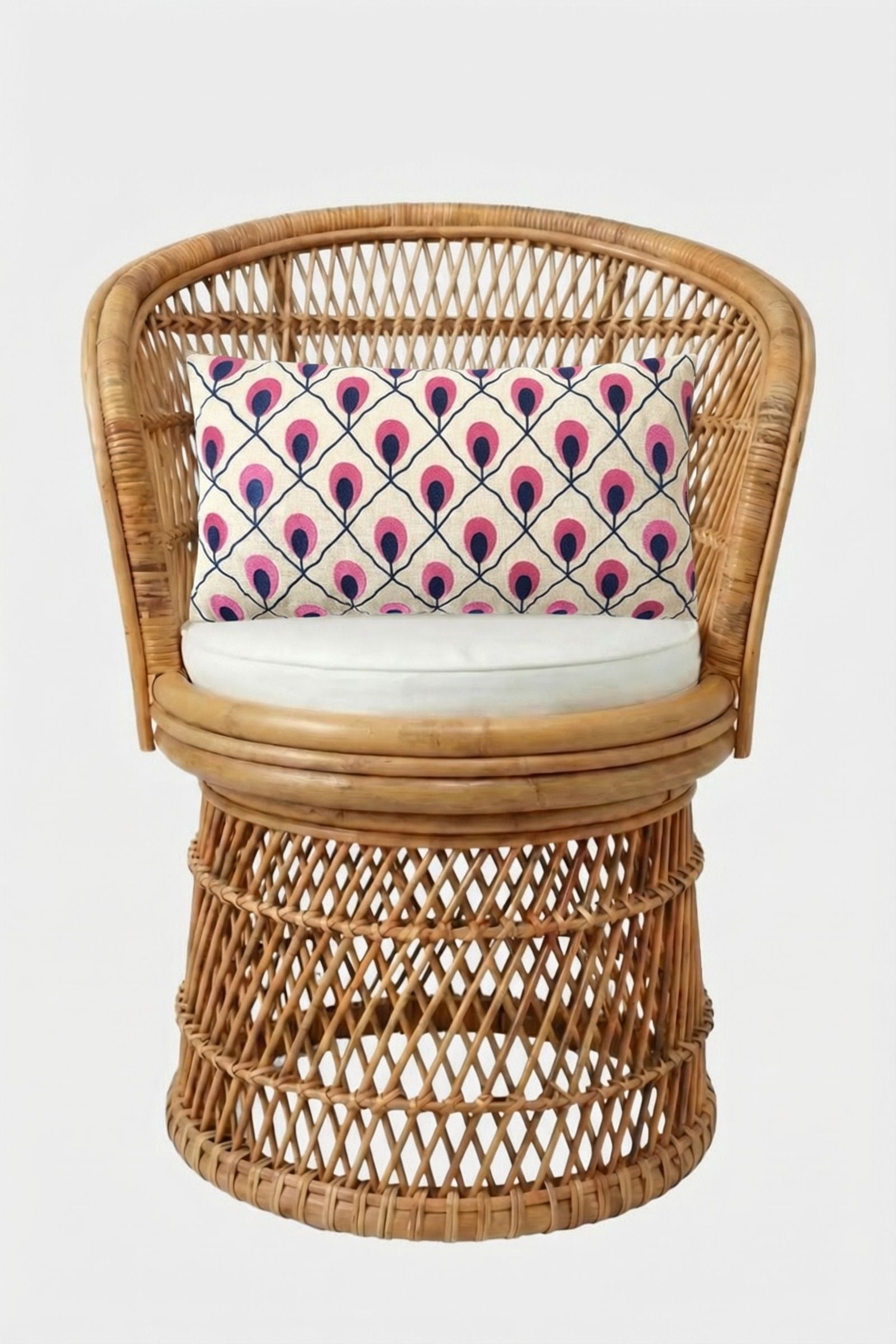 A round wicker chair with a white seat cushion and the Roseville Embroidered Lumbar Pillow, which features a pink and blue geometric peacock feather pattern, set against a plain white background.