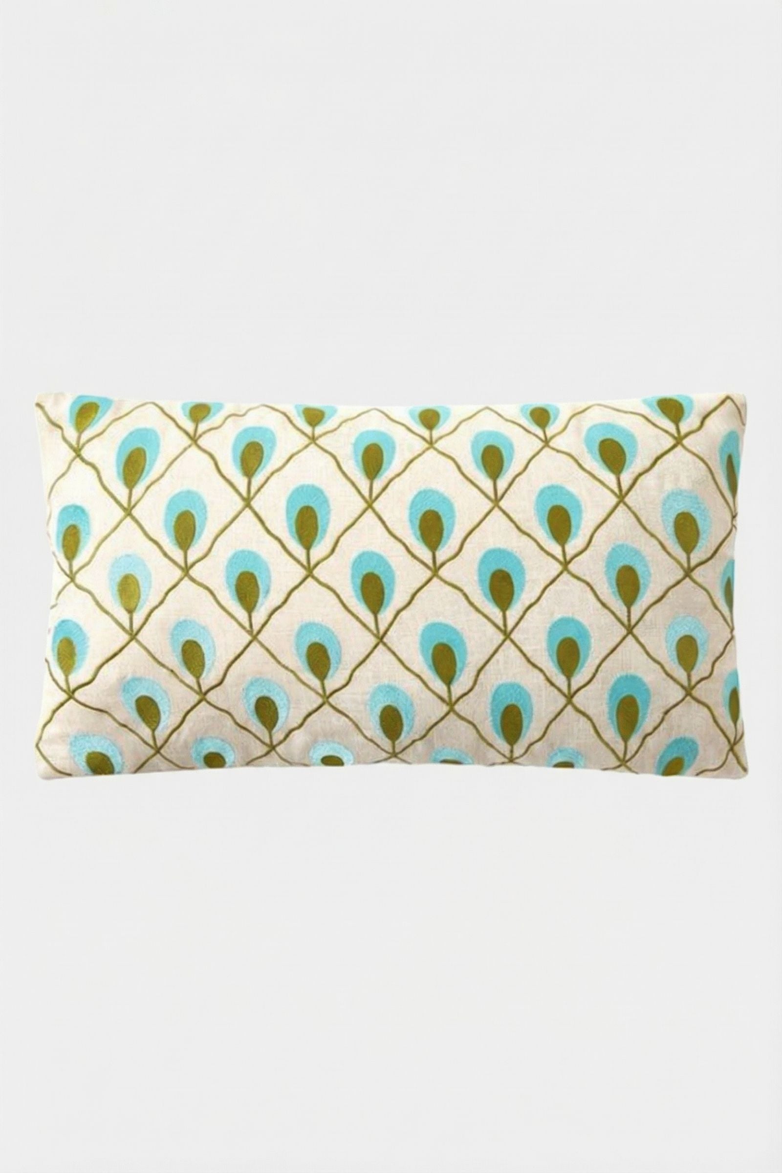 The Roseville Embroidered Lumbar Pillow features a white background with a diamond grid of stylized peacock feathers in teal, blue, and gold.