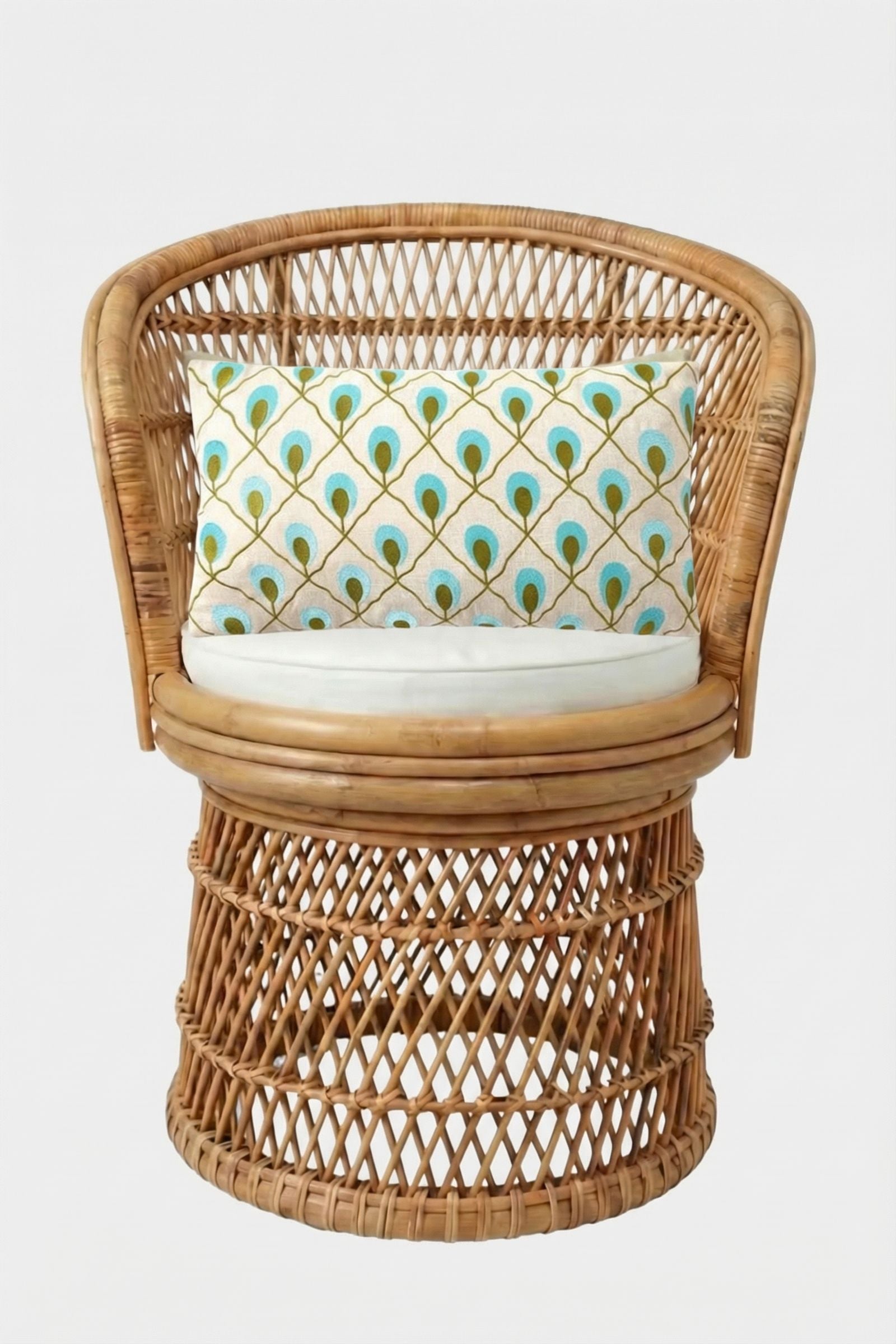 A round wicker chair with a curved back and open weave, featuring a white seat cushion and the Roseville Embroidered Lumbar Pillow, which displays a peacock feather pattern in blue, green, and gold.