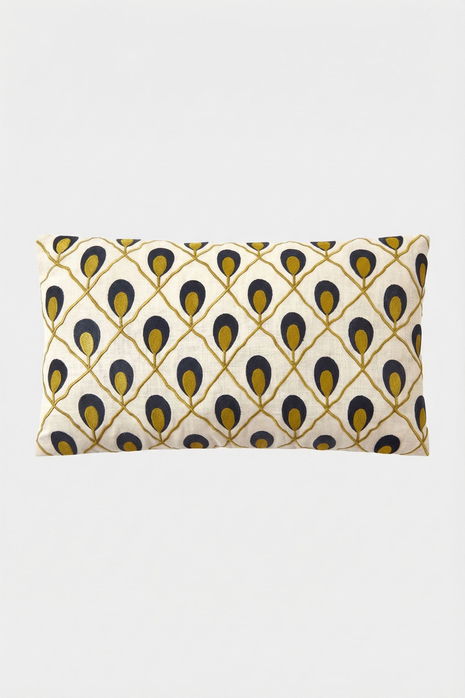 The Roseville Embroidered Lumbar Pillow is cream-colored with a diagonal grid of navy blue and gold peacock feather motifs on a plain white background.