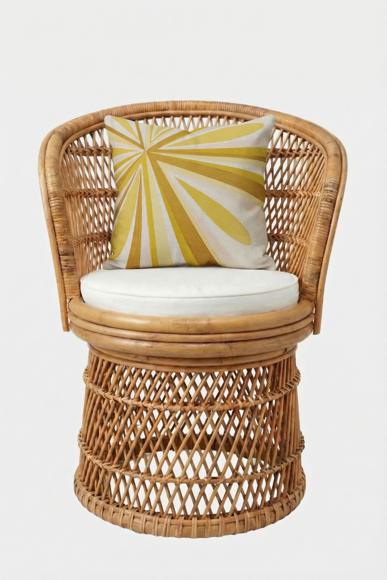 A round wicker chair with a white cushion and the Shante Embroidered Pillow, which displays a yellow and white sunburst design, set against a plain white background.