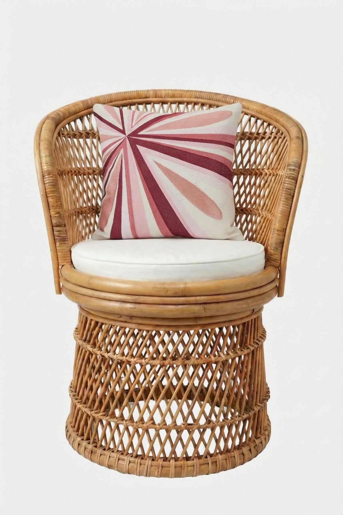 A round rattan chair with an open-weave design, white seat cushion, and the Shante Embroidered Square Pillow featuring bold pink and red geometric lines on white, set against a plain white backdrop.