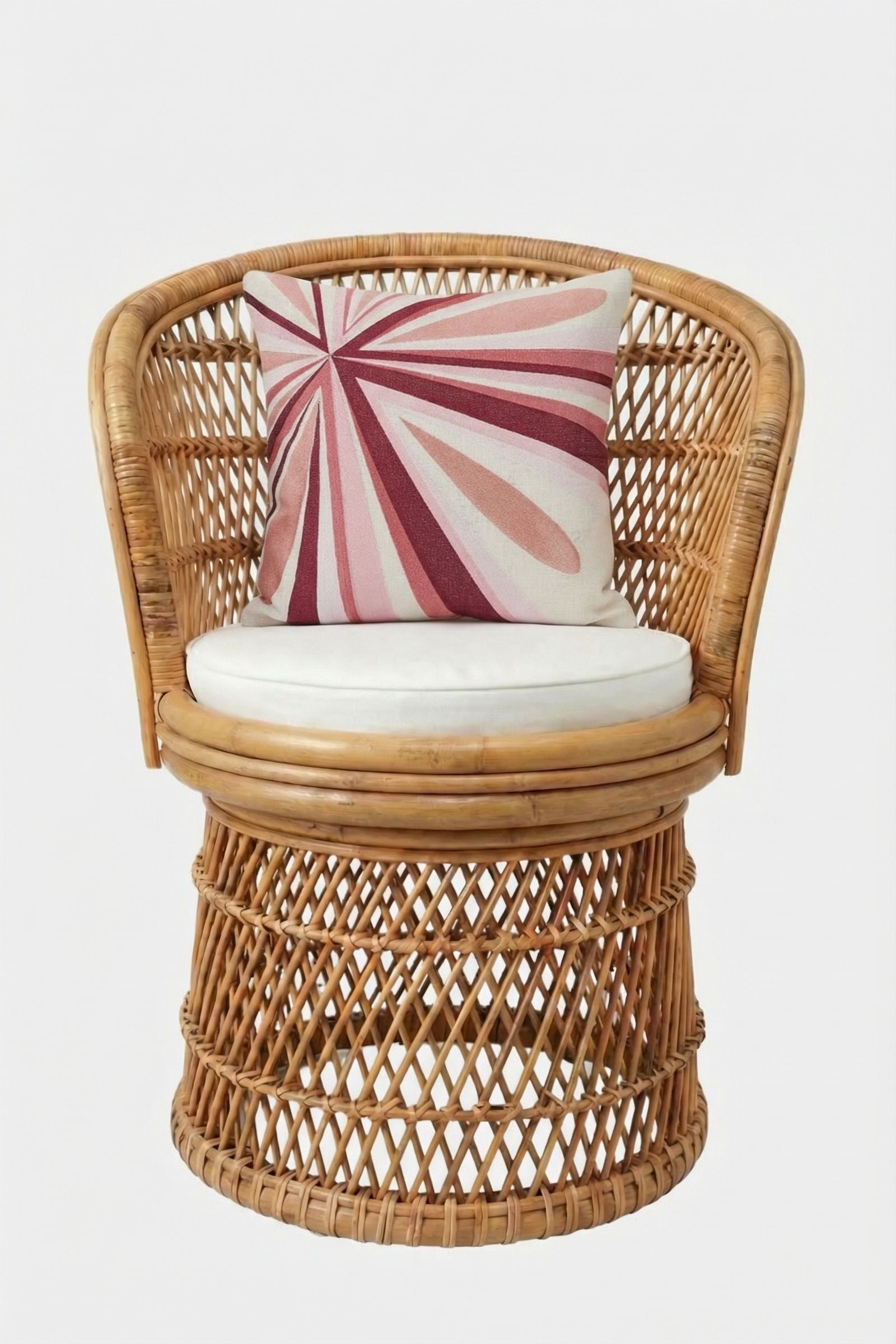 A round rattan chair with an open-weave design, white seat cushion, and the Shante Embroidered Square Pillow featuring bold pink and red geometric lines on white, set against a plain white backdrop.