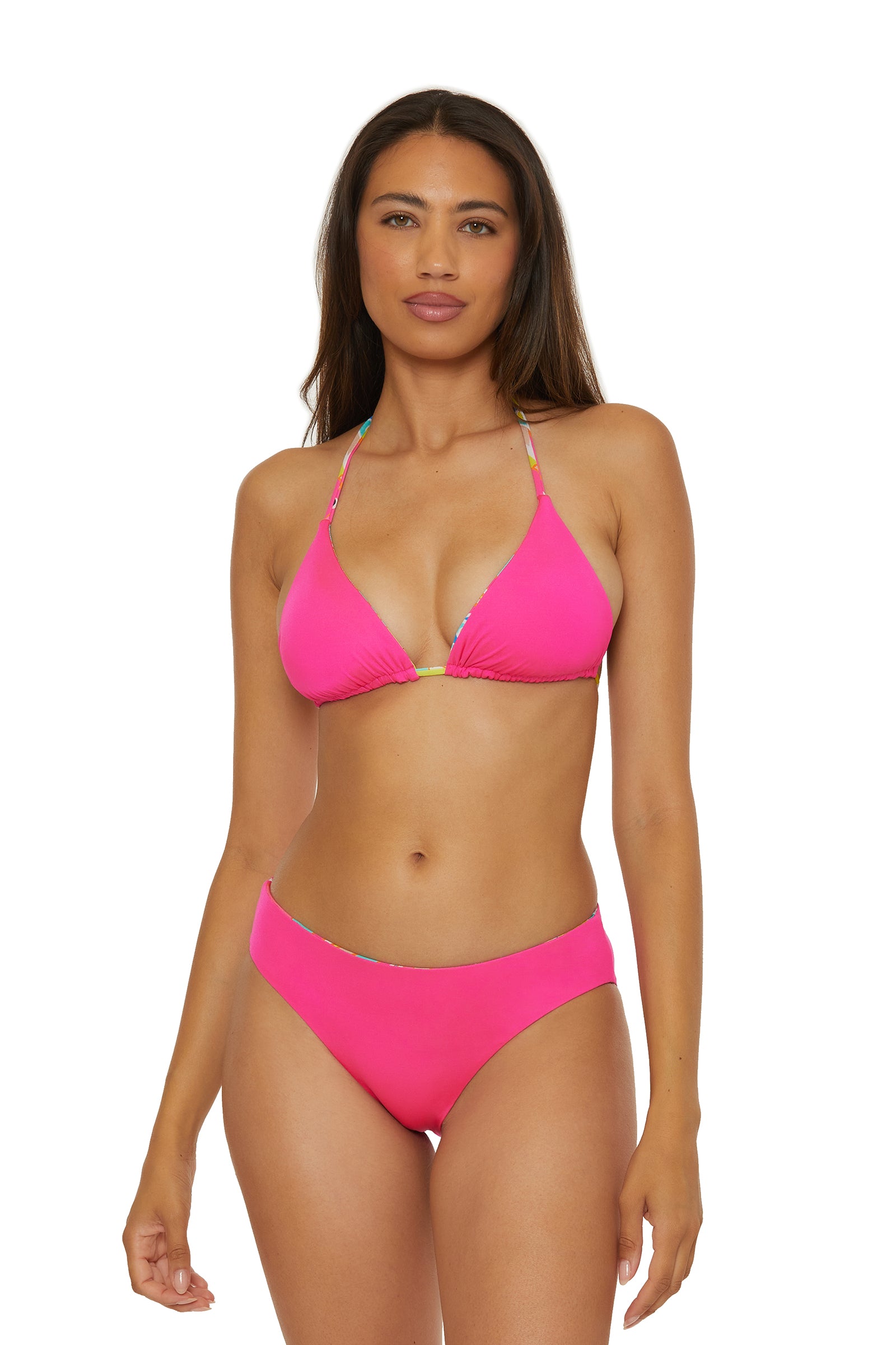 A woman with long brown hair models the Reversible Hipster Swim Bottom - Venus in bright pink, standing against a white background facing forward with a neutral expression and her left arm by her side.