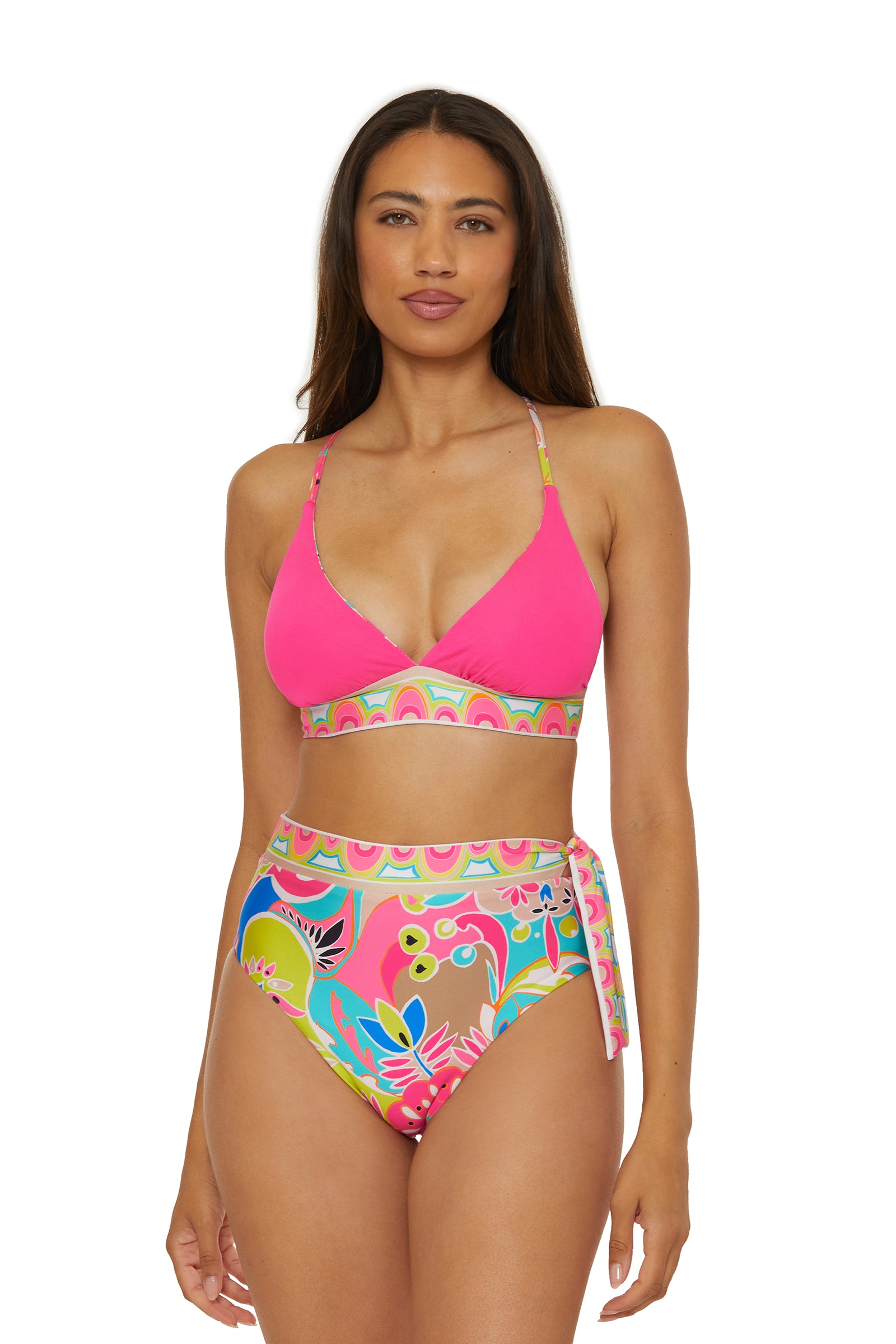 A woman with long brown hair and a neutral expression wears the Venus Reversible Halter Bra Swim Top in pink, featuring a patterned band, paired with high-waisted, colorful floral side-tie bikini bottoms.