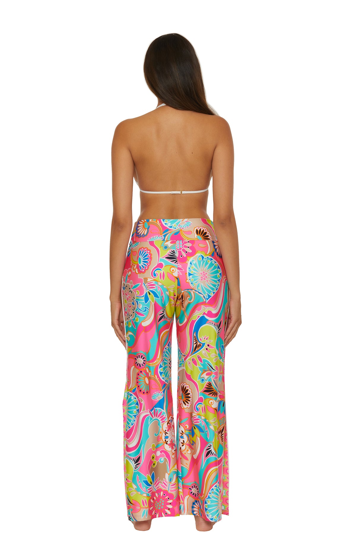 A woman stands with her back to the camera, wearing a white halter bikini top paired with the Swim Cover-Up Pant - Venus—high-waisted, wide-leg pants featuring a colorful, abstract floral print.