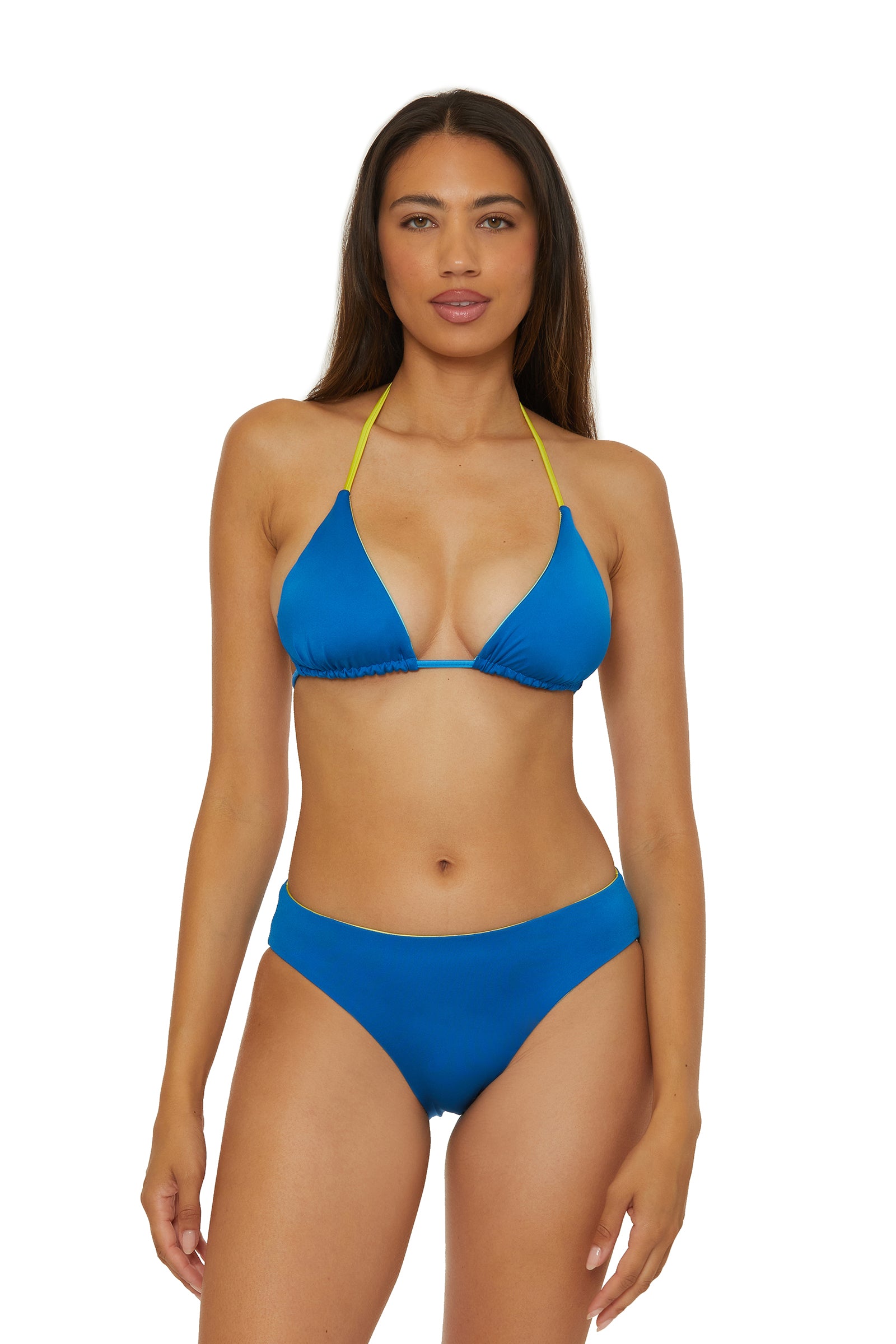 A woman with long brown hair wears the Reversible Hipster Swim Bottom - West Palm, featuring blue fabric with yellow straps, standing against a white background and looking at the camera with a neutral expression.