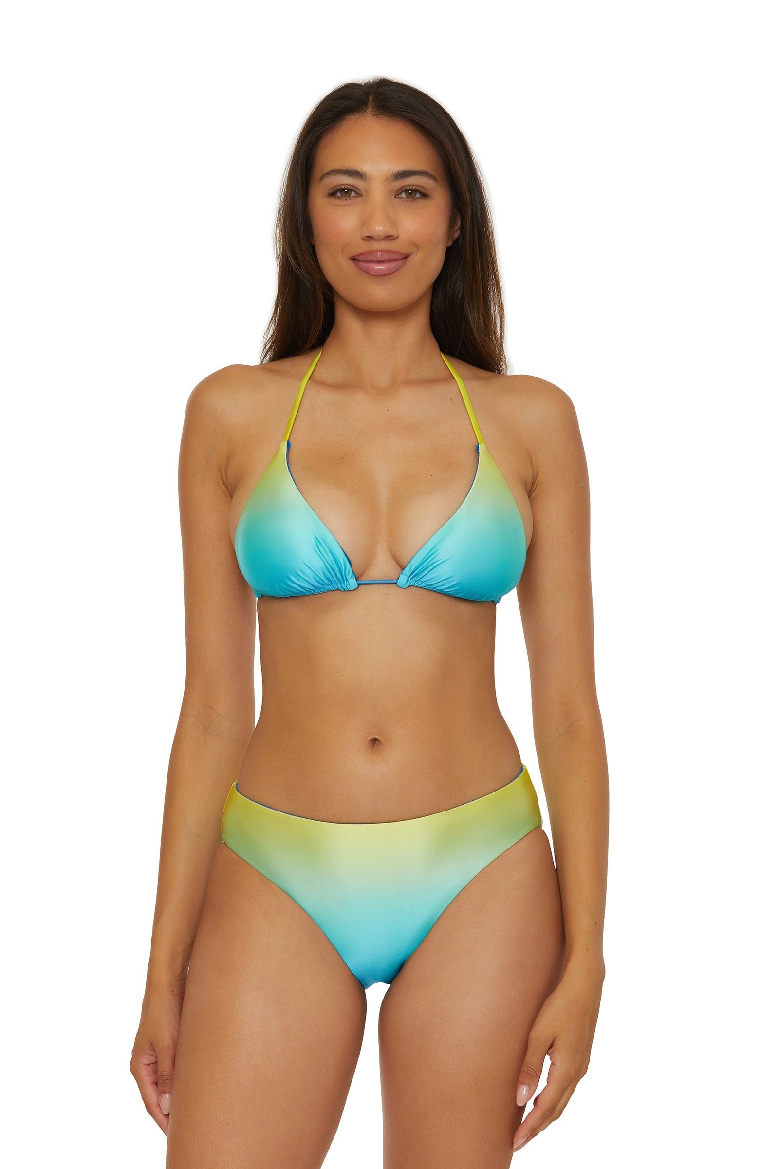 A woman faces forward, smiling slightly, wearing the Reversible Hipster Swim Bottom - West Palm with a blue and yellow gradient bikini against a plain white background.