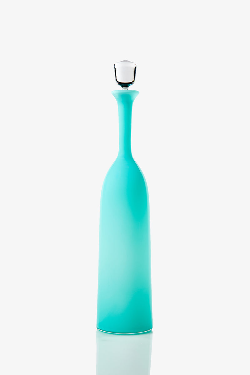 The Wexler Tall Bottle is a tall, slender turquoise vessel featuring a narrow neck and a white stopper, shown standing upright against a plain white background.