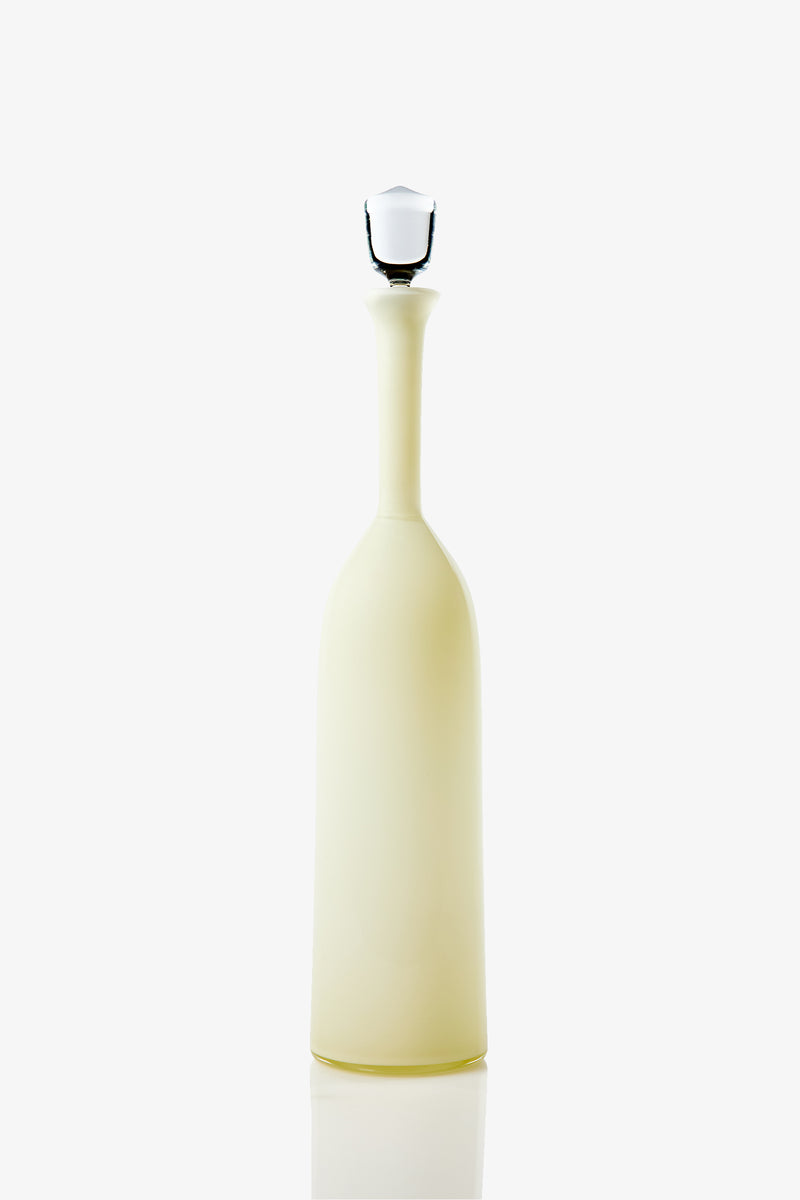 The Wexler Tall Bottle is a tall, slender, opaque pale yellow vessel with a long neck and a white stopper, photographed against a plain white background.