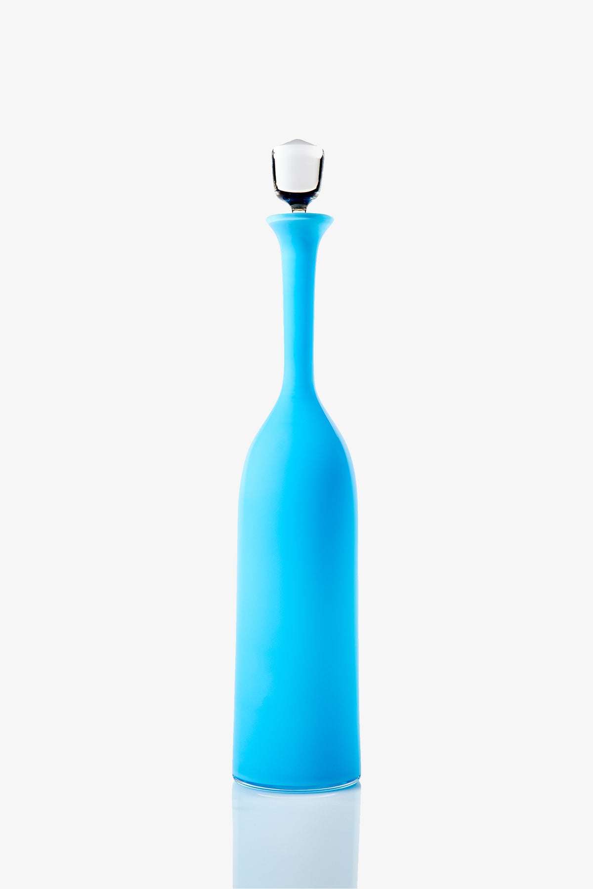 The Wexler Tall Bottle, featuring a sleek blue design with a narrow neck and white stopper, stands upright on a reflective surface against a plain white background.
