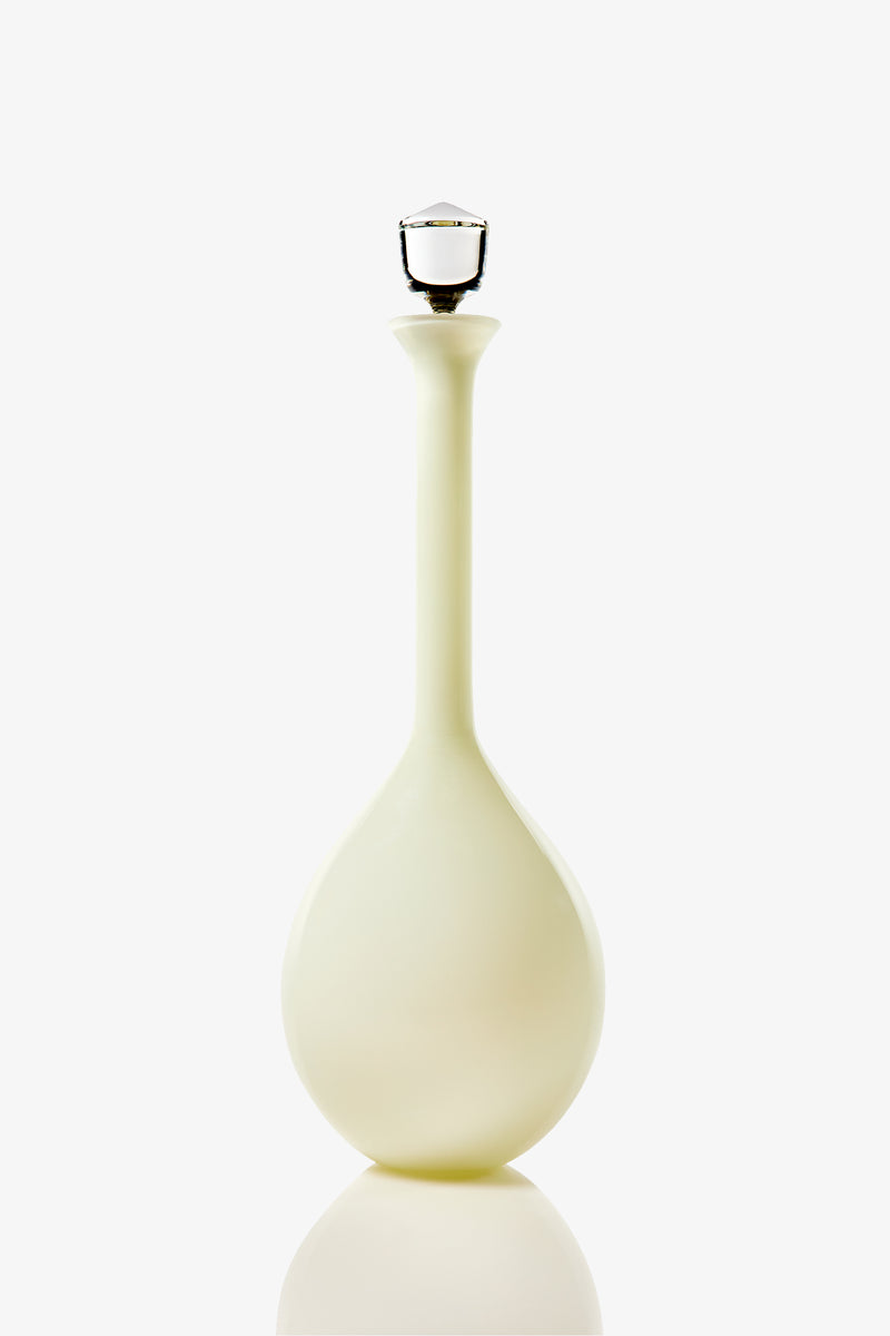 A tall and elegant Wexler Tear Drop Bottle, crafted from opaque white glass with a round base, a slender neck, and finished with a clear glass stopper, is displayed against a plain white background.