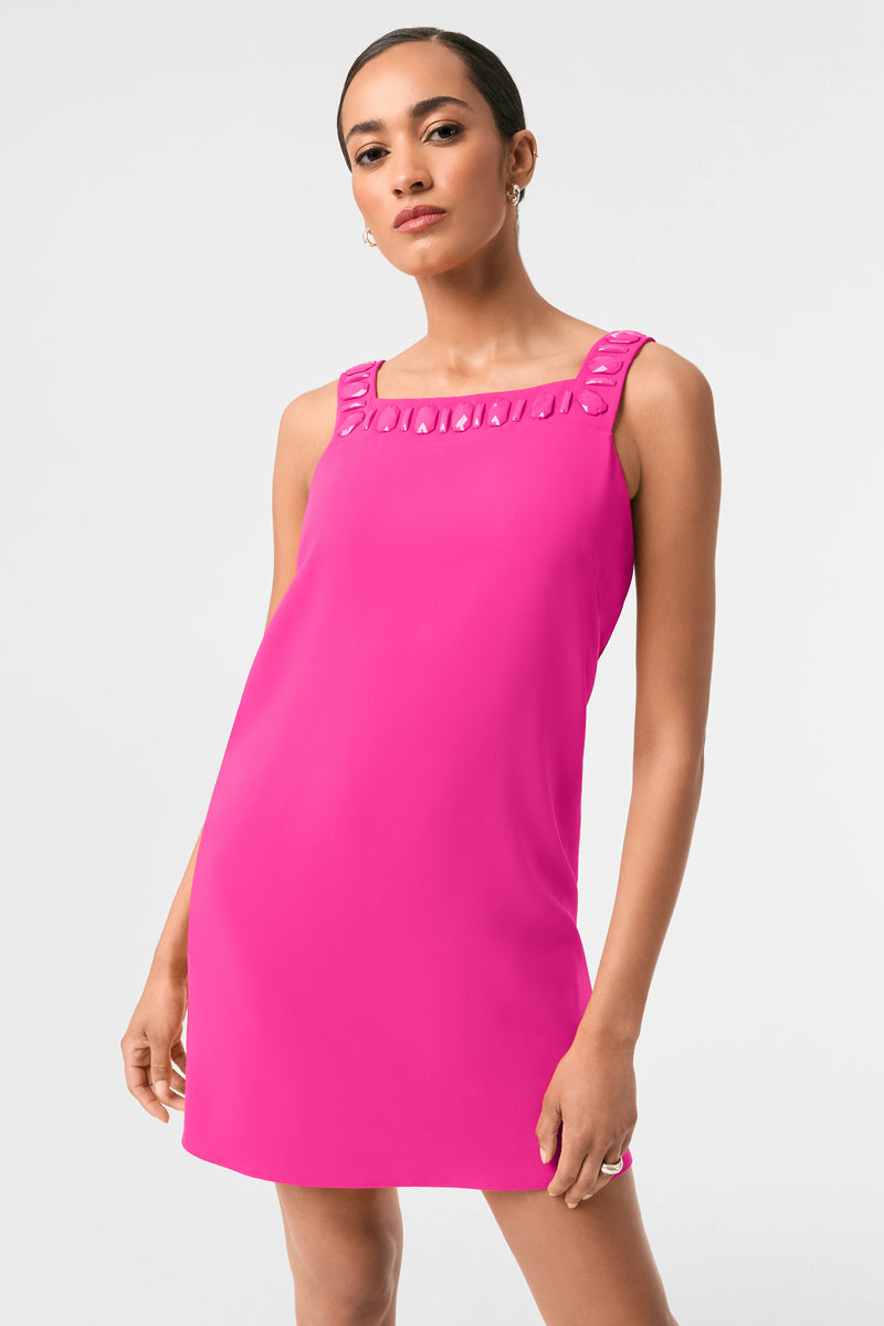 A woman poses in the Yokuna Jewel Neck Mini Dress, a sleeveless bright pink mini dress with a square neckline and decorative collar details, set against a plain light gray background.