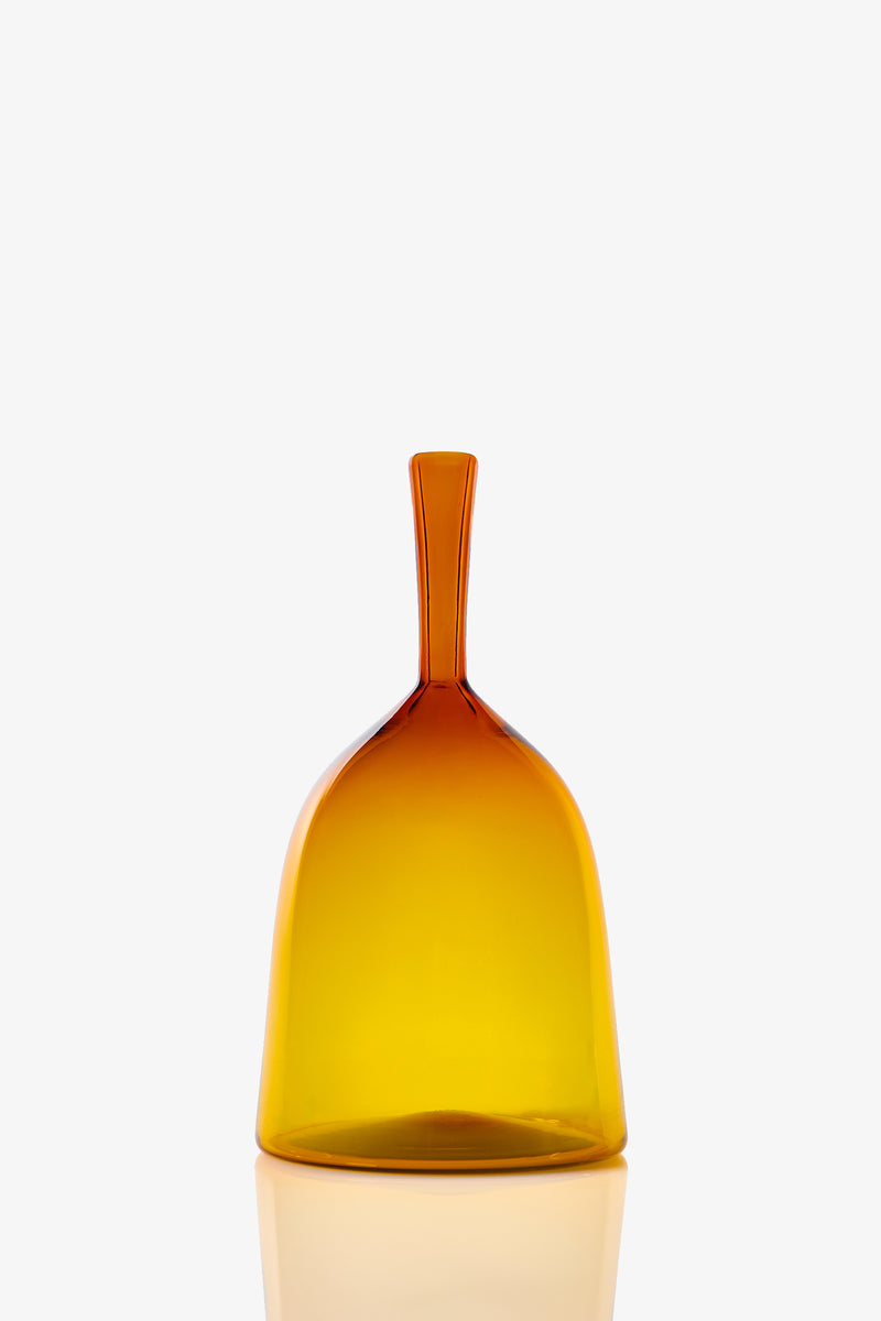 The Wide Angelic Bottle is a translucent amber glass piece with a smooth, simple shape and a short, narrow handle, showcased against a plain white background.