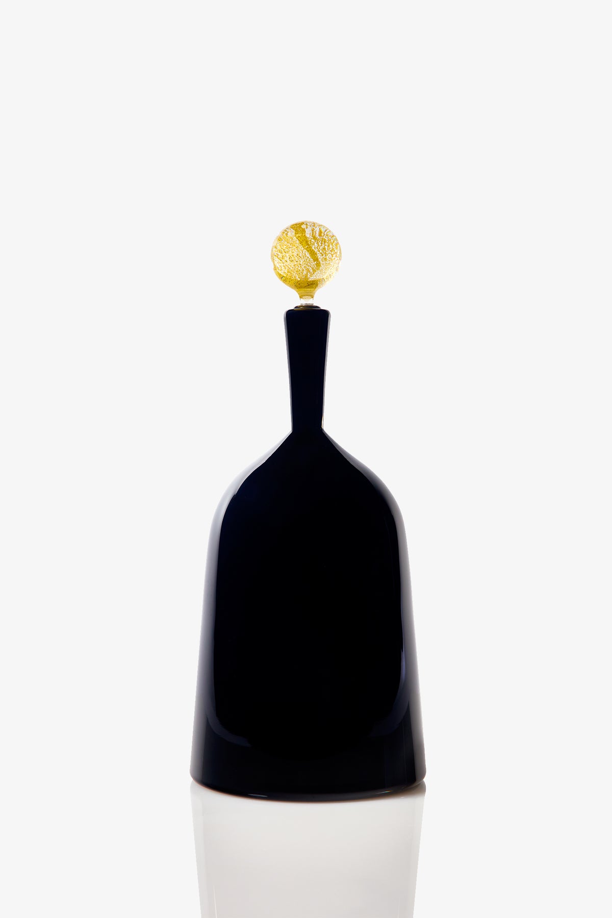 The Wide Bottle Carmella Barware is a sleek, black, bell-shaped glass vessel with a narrow neck and a small, textured golden sphere on top, set against a plain white background.