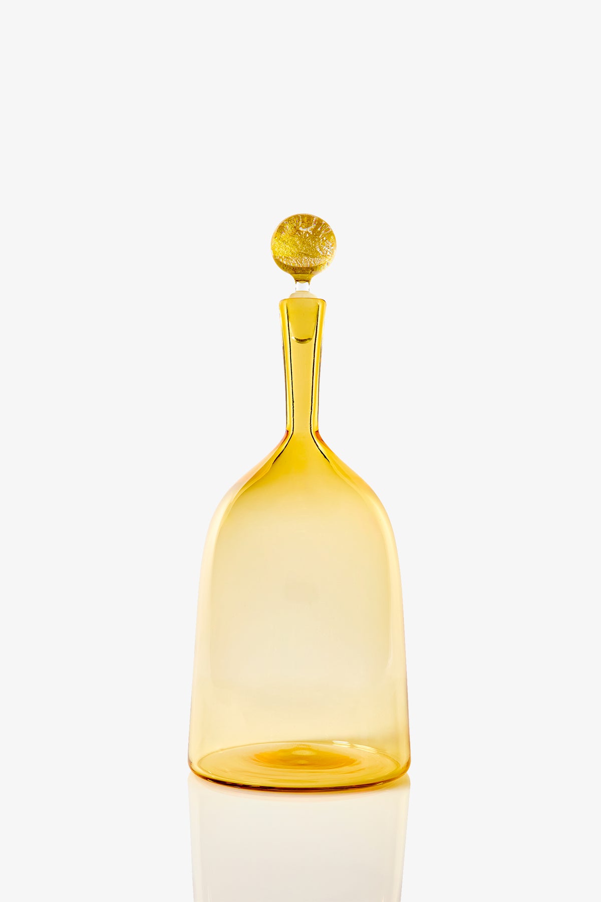 The Wide Bottle Carmella Barware is a translucent amber glass bottle featuring a tall, slender neck and a round matching stopper, displayed against a plain white background.