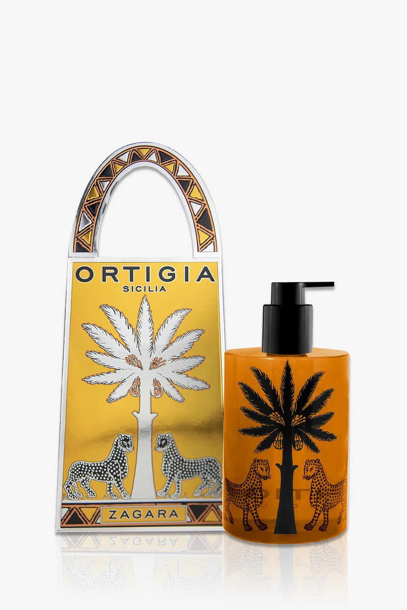 An amber pump bottle of Ortigia Hand Soap, featuring black palm tree and leopard designs, stands beside a matching gold and white gift box labeled "Ortigia Sicilia Zagara," both decorated with leopards and a palm tree.