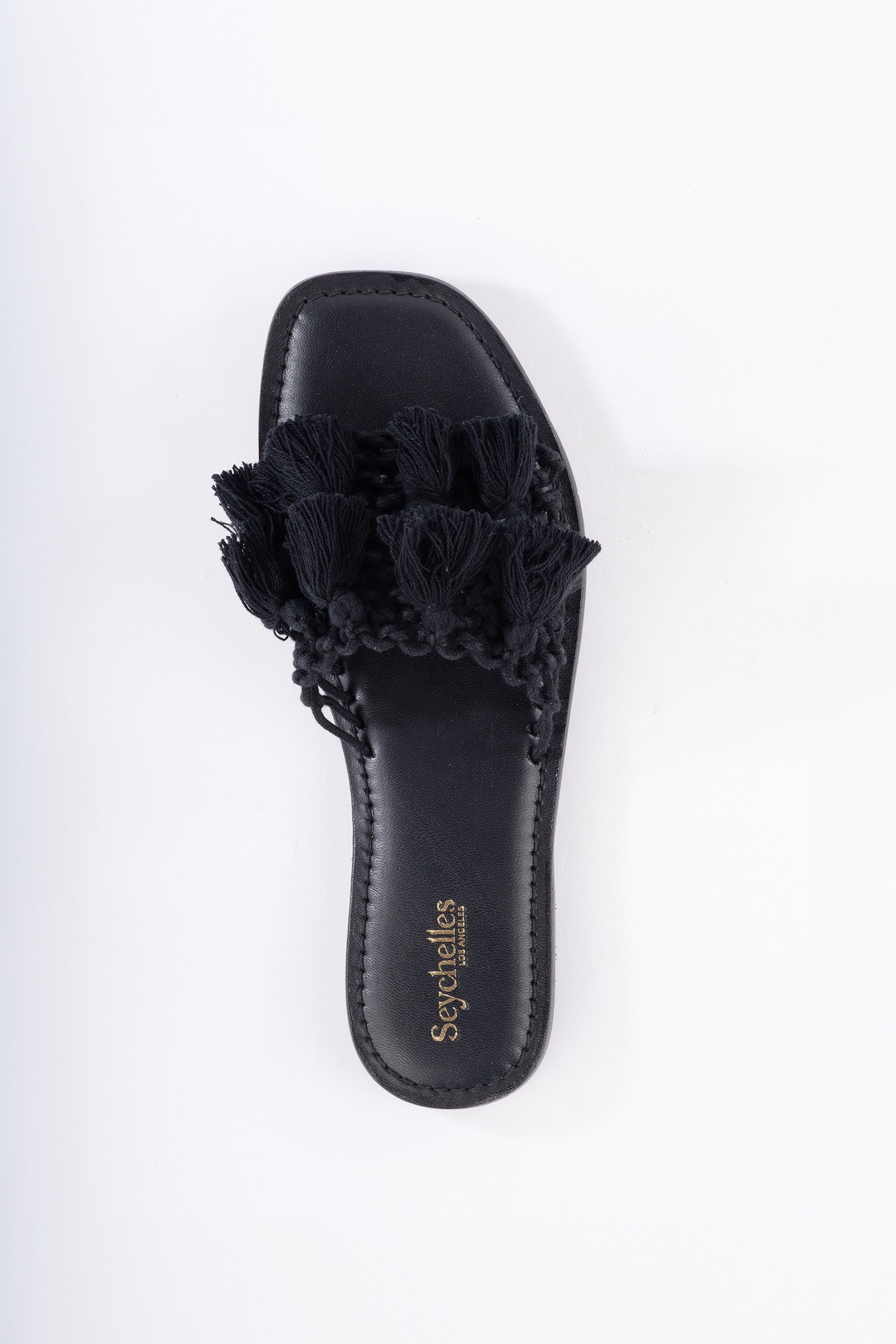 The Seychelles Camellia Slide Sandal is a black open-toe slide with tassels on the upper strap, a cushioned footbed, and gold Seychelles branding on the insole, shown against a white background.
