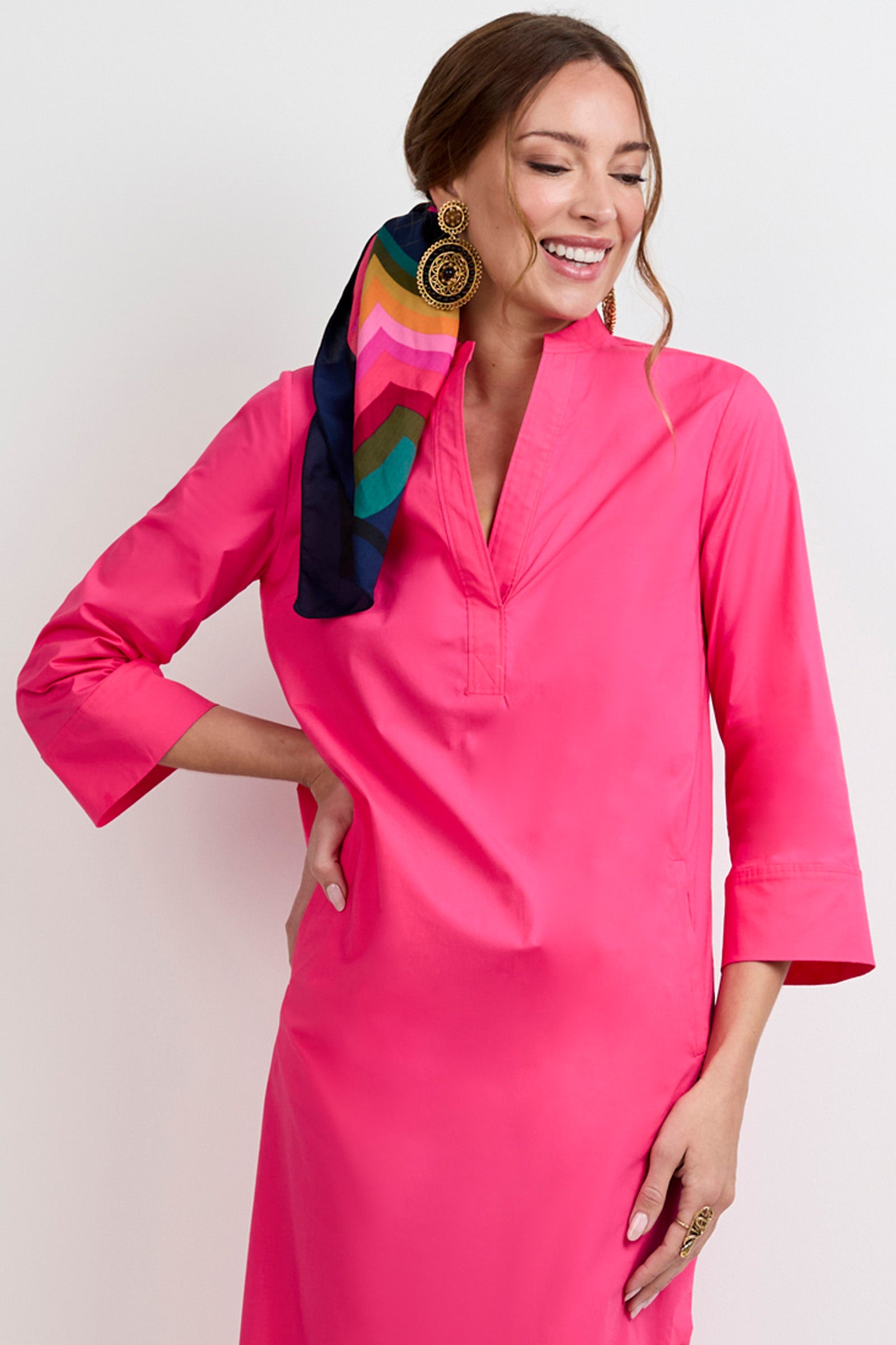 A smiling woman wears the Capella Mandarin Collar Maxi Dress in bright pink, paired with a colorful striped hair scarf and large gold earrings, standing against a light background.