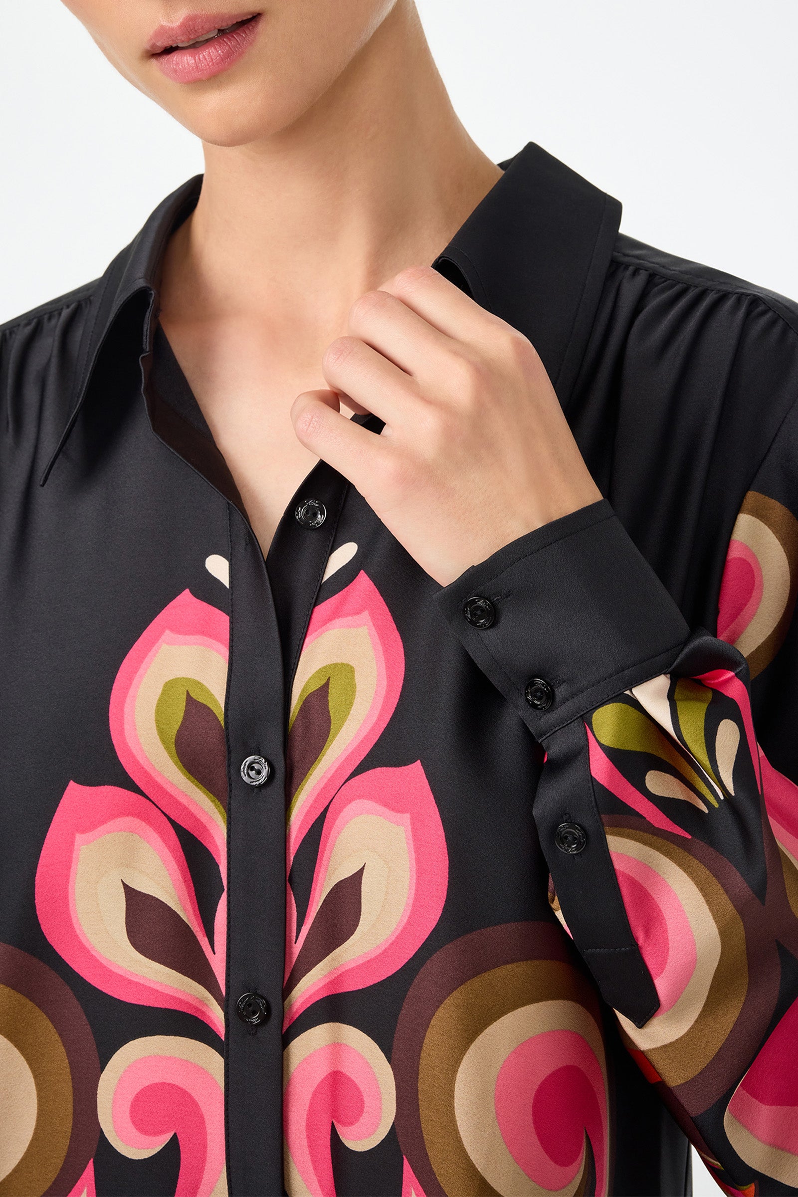A woman wearing the Cassavetes Border Shirt - Sanctuary, a black button-up with a bold abstract floral pattern in pink, brown, green, and beige, adjusts her collar. The image is cropped to show her upper torso.