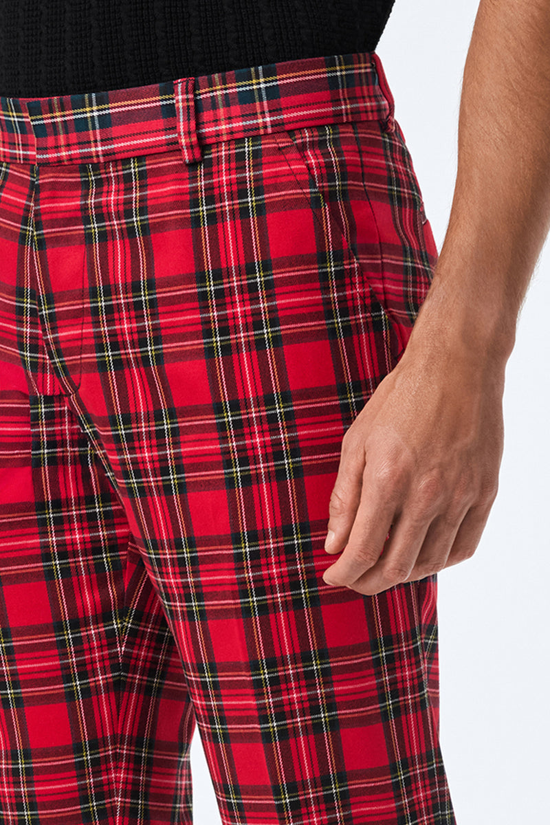 A person stands with their right arm relaxed, wearing the Clyde Slim Trouser - Can-Can Check in a red plaid pattern with black, white, and yellow stripes, paired with a black top.