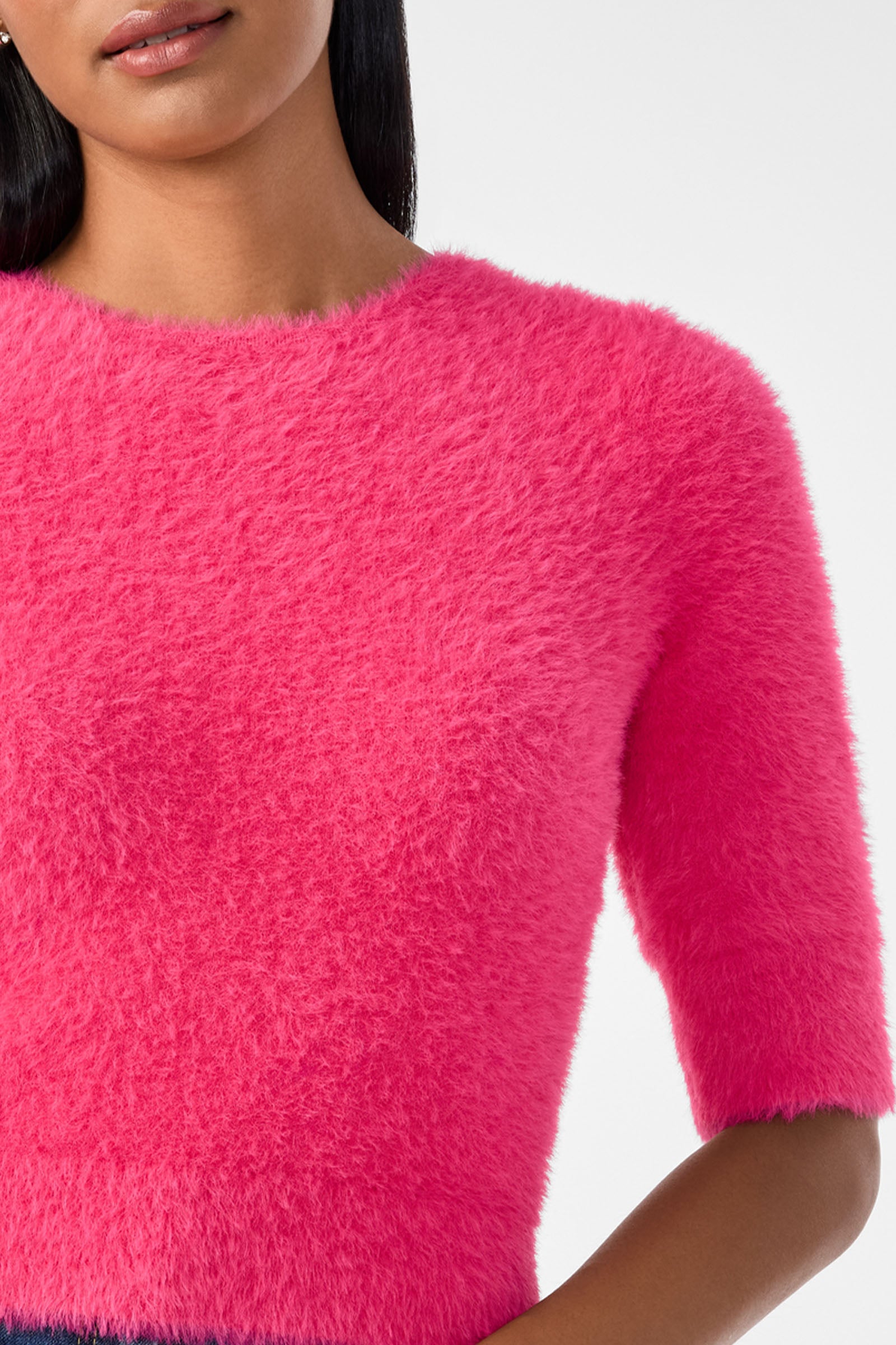 A woman models the Maliah Fuzzy Sweater in bright pink, featuring short sleeves and a soft, fuzzy texture. The photo shows her from shoulders to waist with her head partially visible against a plain white background.