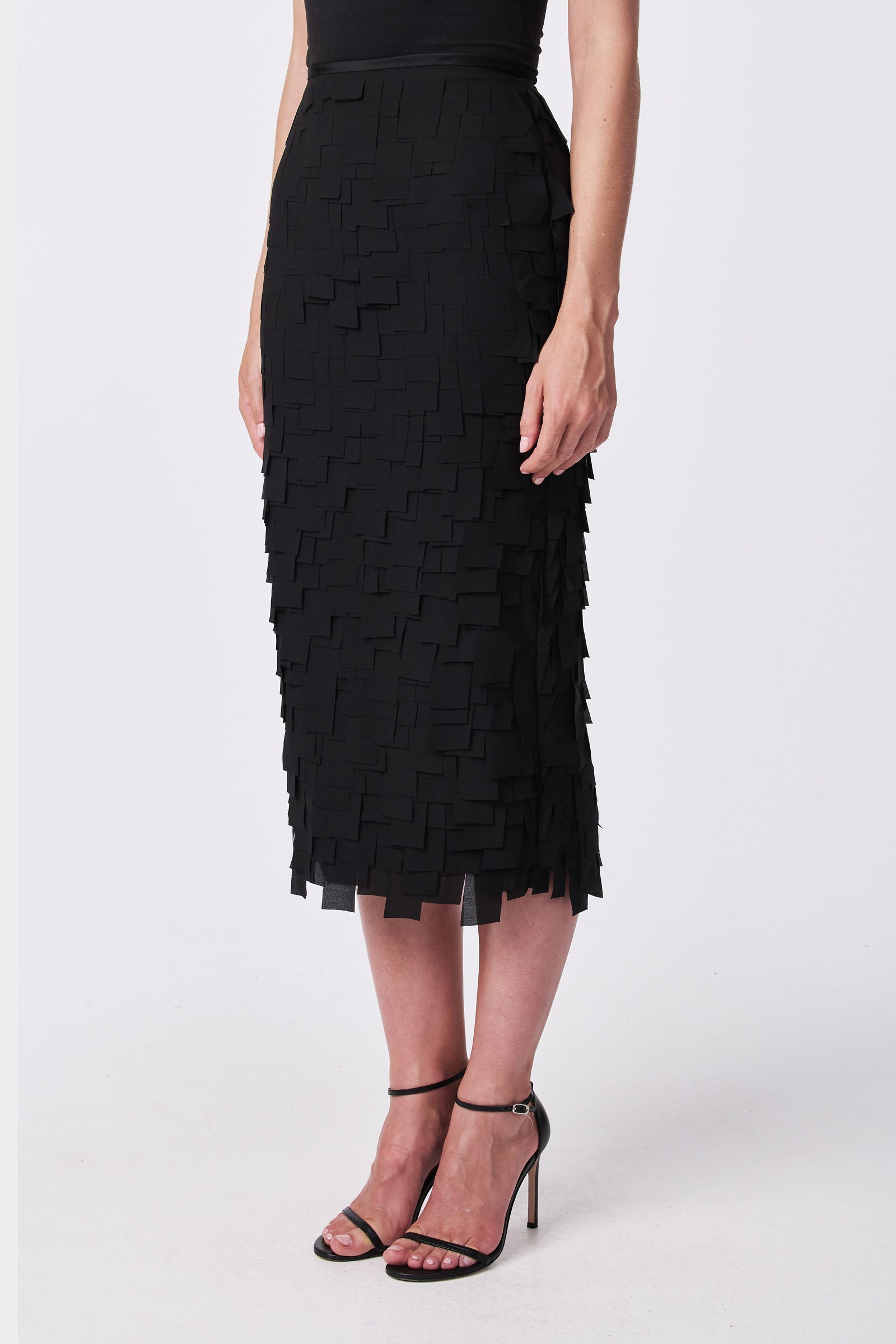 A woman wears the Dita Midi Pencil Skirt - Flutter Chiffon with black high-heeled sandals, posing against a plain white background.