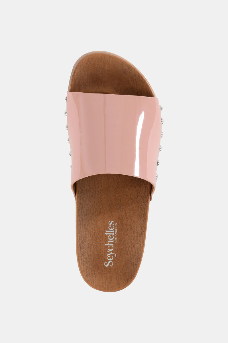 The Seychelles Fantasy Patnt Slide features a glossy light pink wide strap over a brown faux-wood sole, with "Seychelles" printed in white on the insole.
