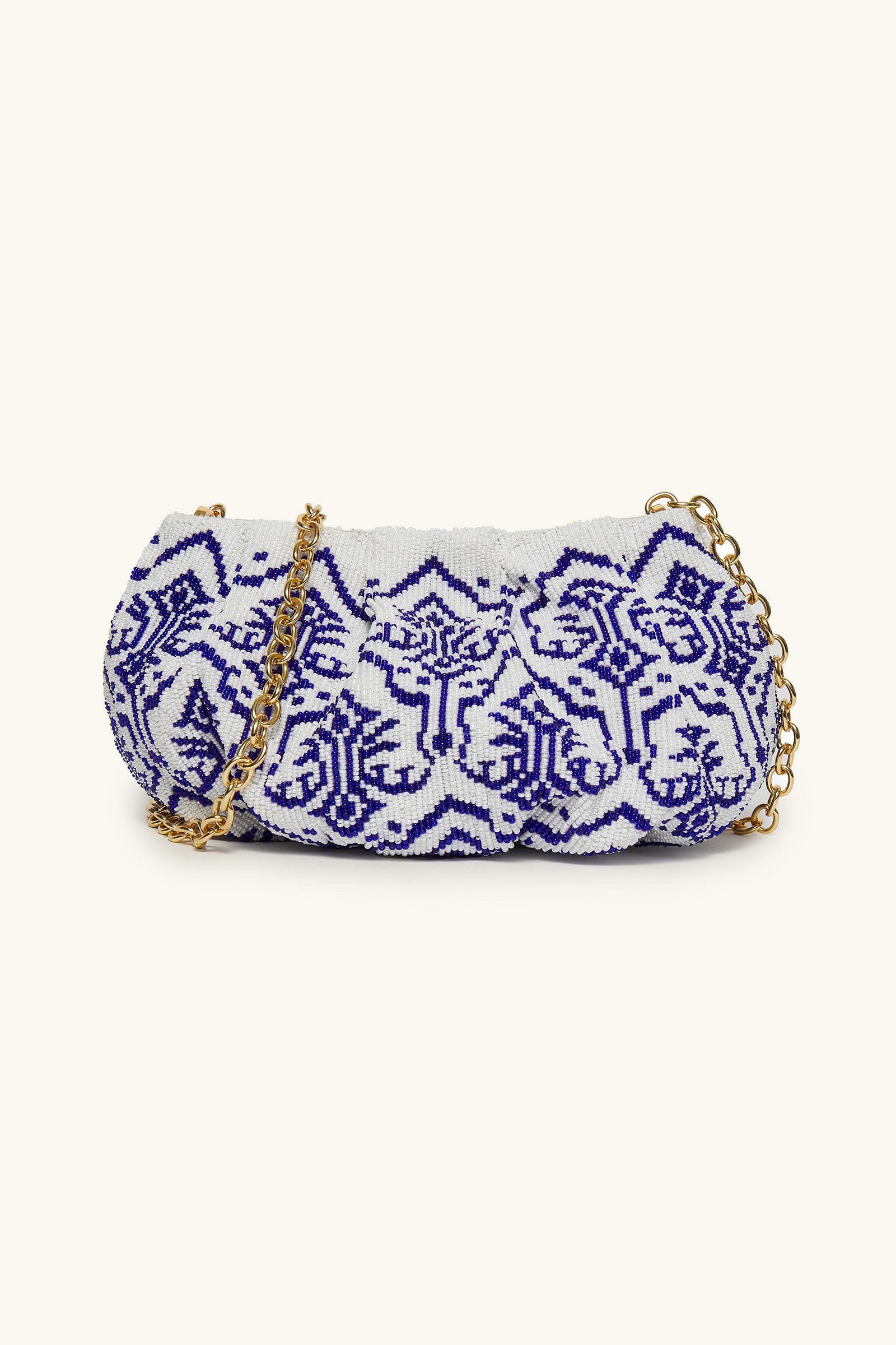 The Blue Ivory Cora Bead Clutch is a small white bag featuring intricate blue geometric beadwork and a gold chain strap, shown against a simple light background.