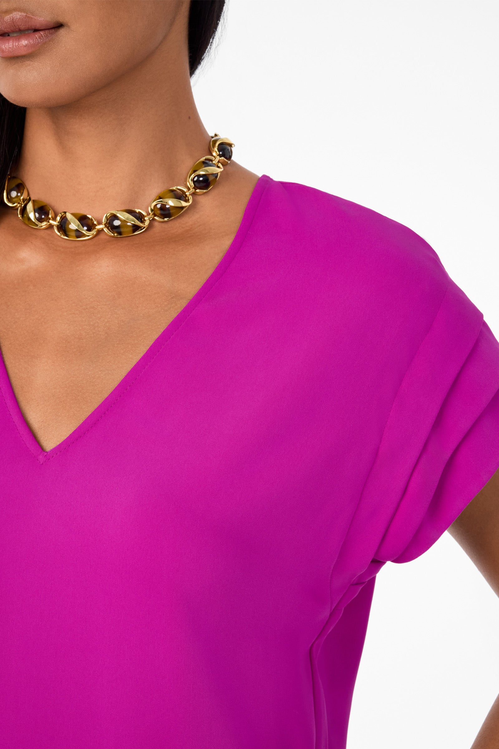A woman wearing a bright magenta V-neck blouse and an Oval Tortoise Necklace, her arm slightly bent and only the lower half of her face visible.