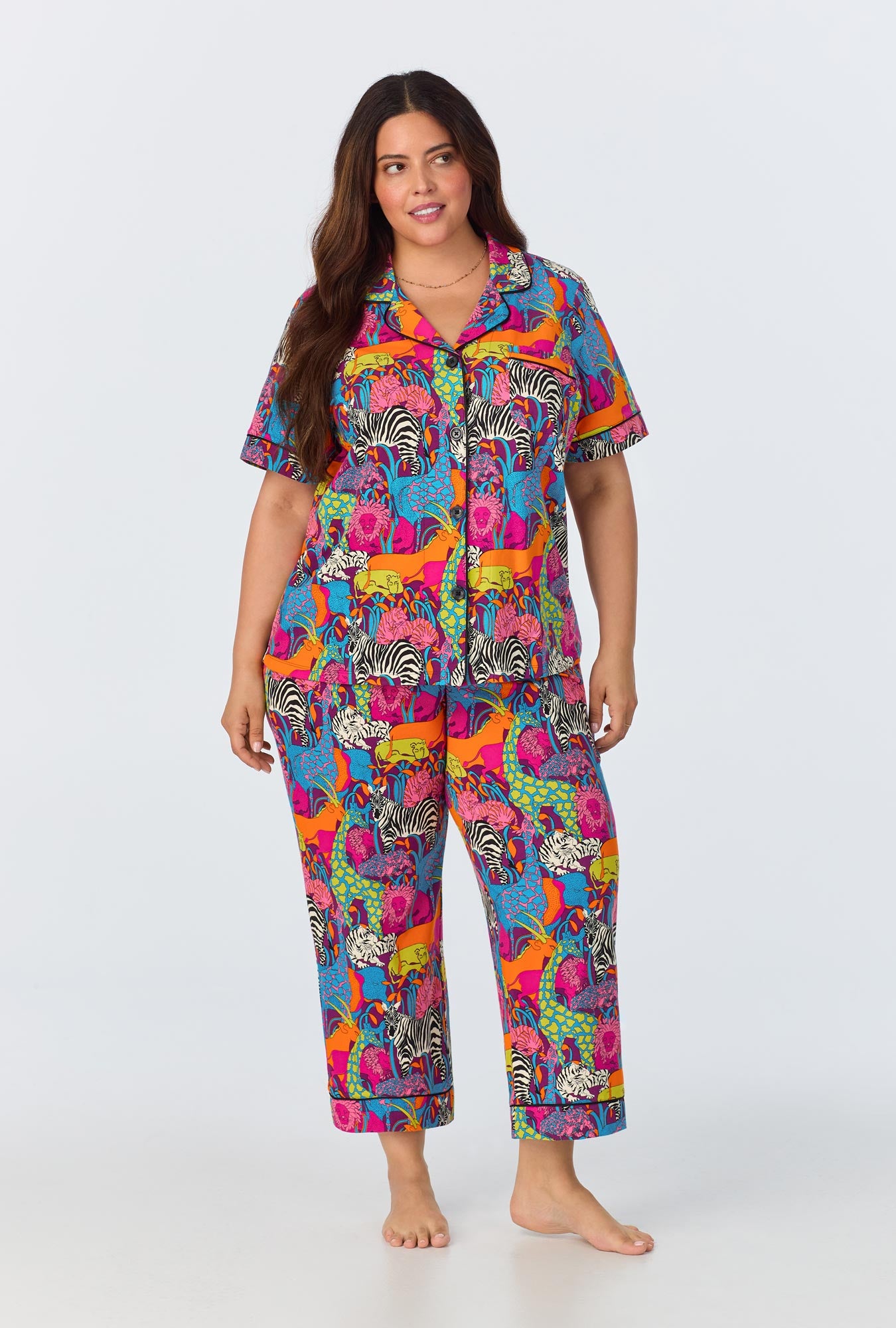 A woman with long brown hair models the Jungle Womens Short Sleeve Cropped Pant Jersey PJ Set in Multi, standing barefoot against a plain white background.