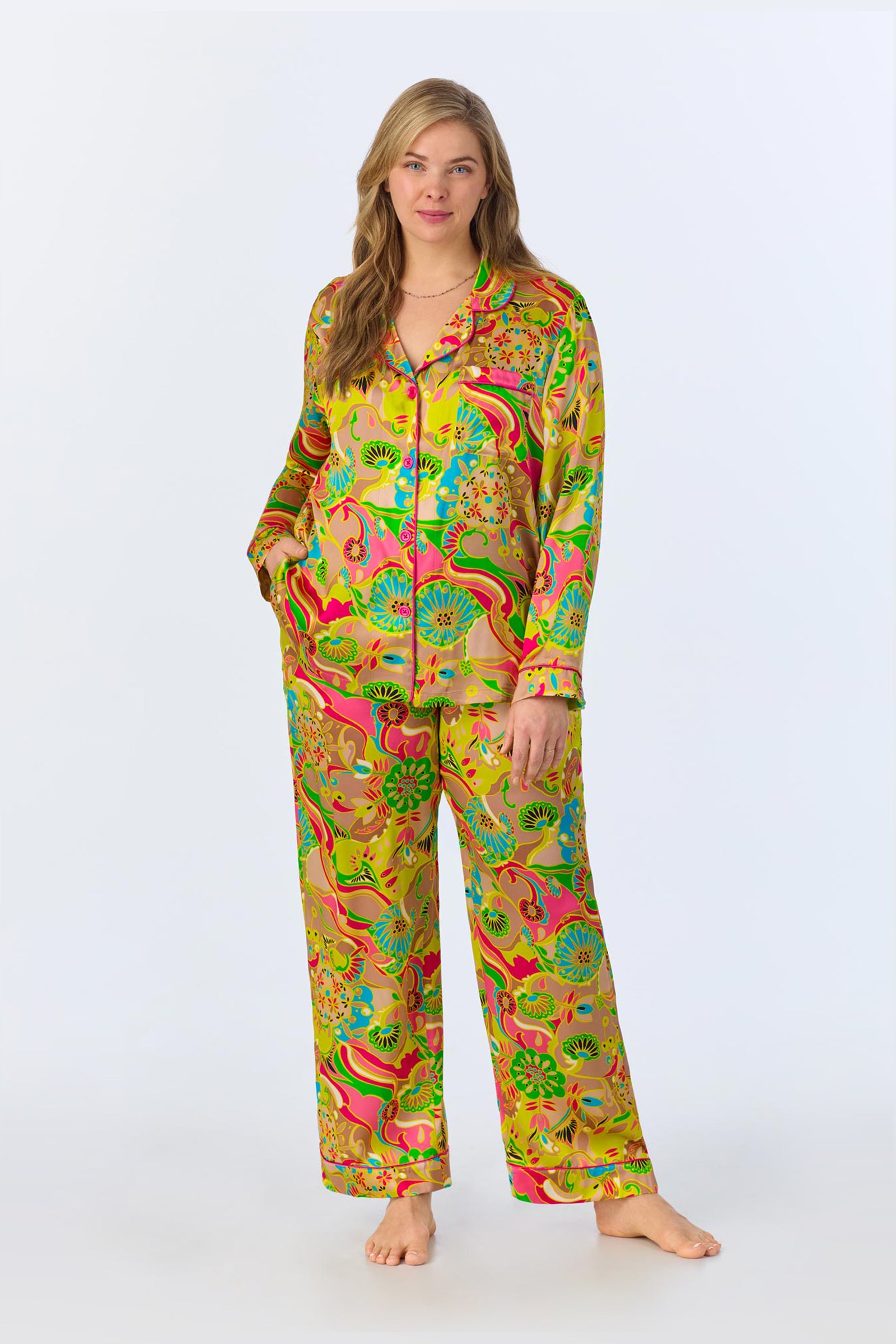 A woman stands barefoot against a plain background wearing the TT LS Pant PJ Set - Heritage Silk, featuring colorful, patterned satin with a button-up shirt and long pants in vibrant floral and abstract designs.
