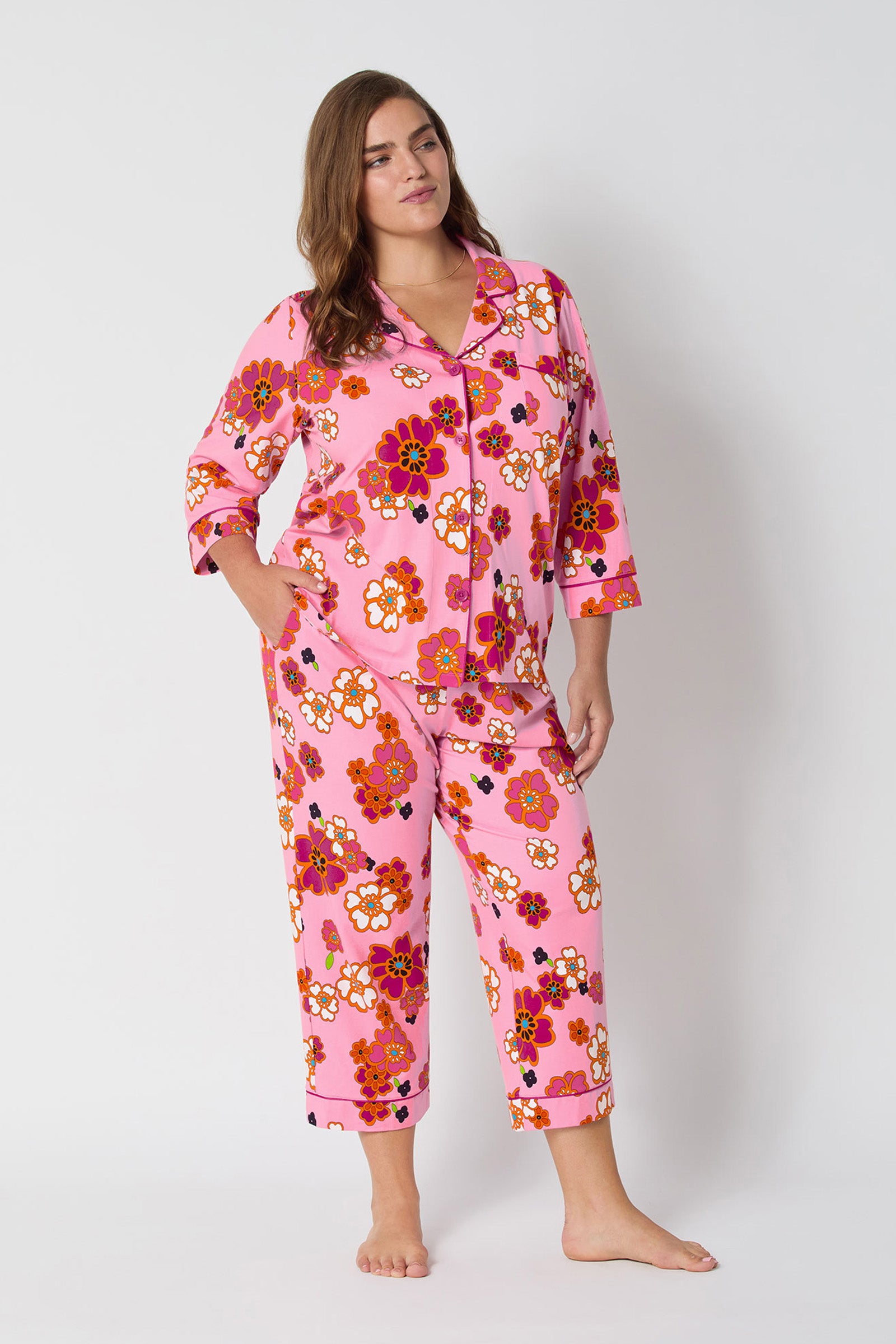 A woman stands barefoot against a plain white background, wearing the Resort Floral 3/4 Cropped Pj featuring a pink floral-print button-up top and matching cropped pants.