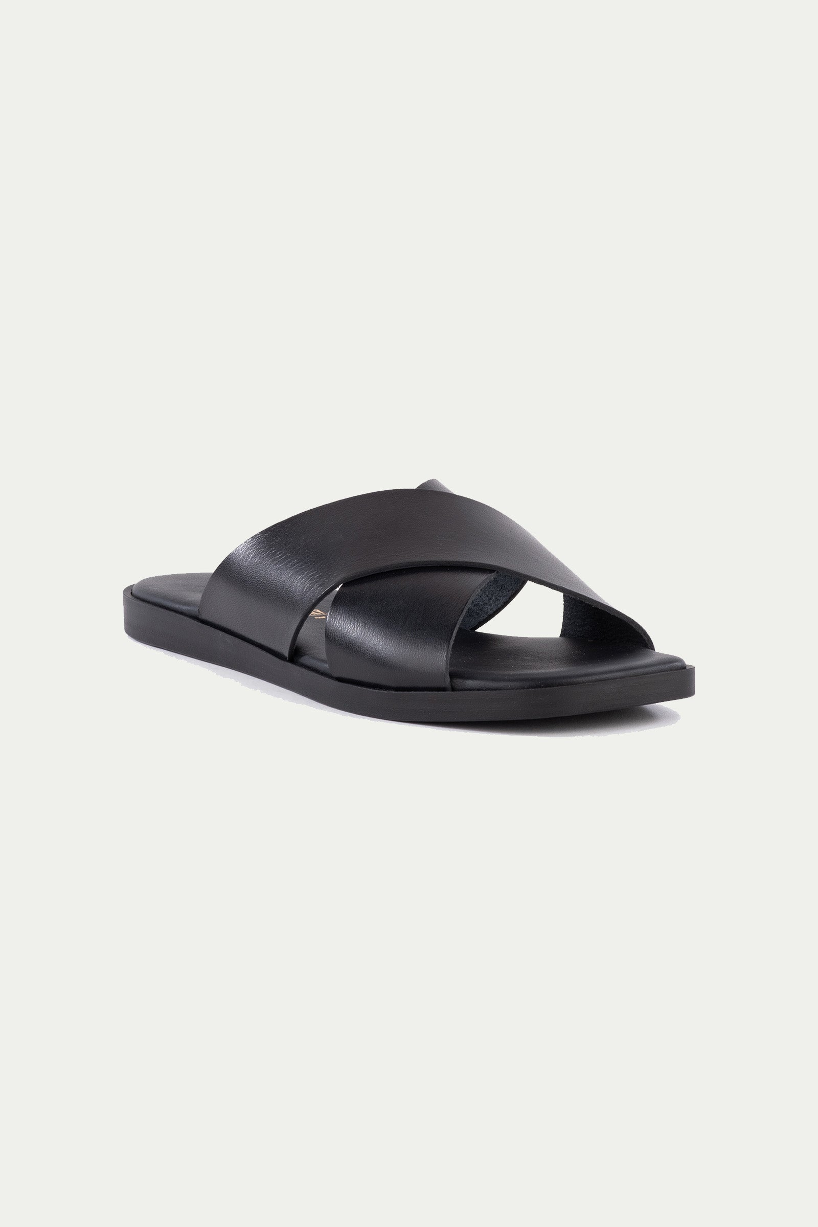 The Chai Sandal in black leather features wide crisscross straps and a flat sole, shown against a plain white background.