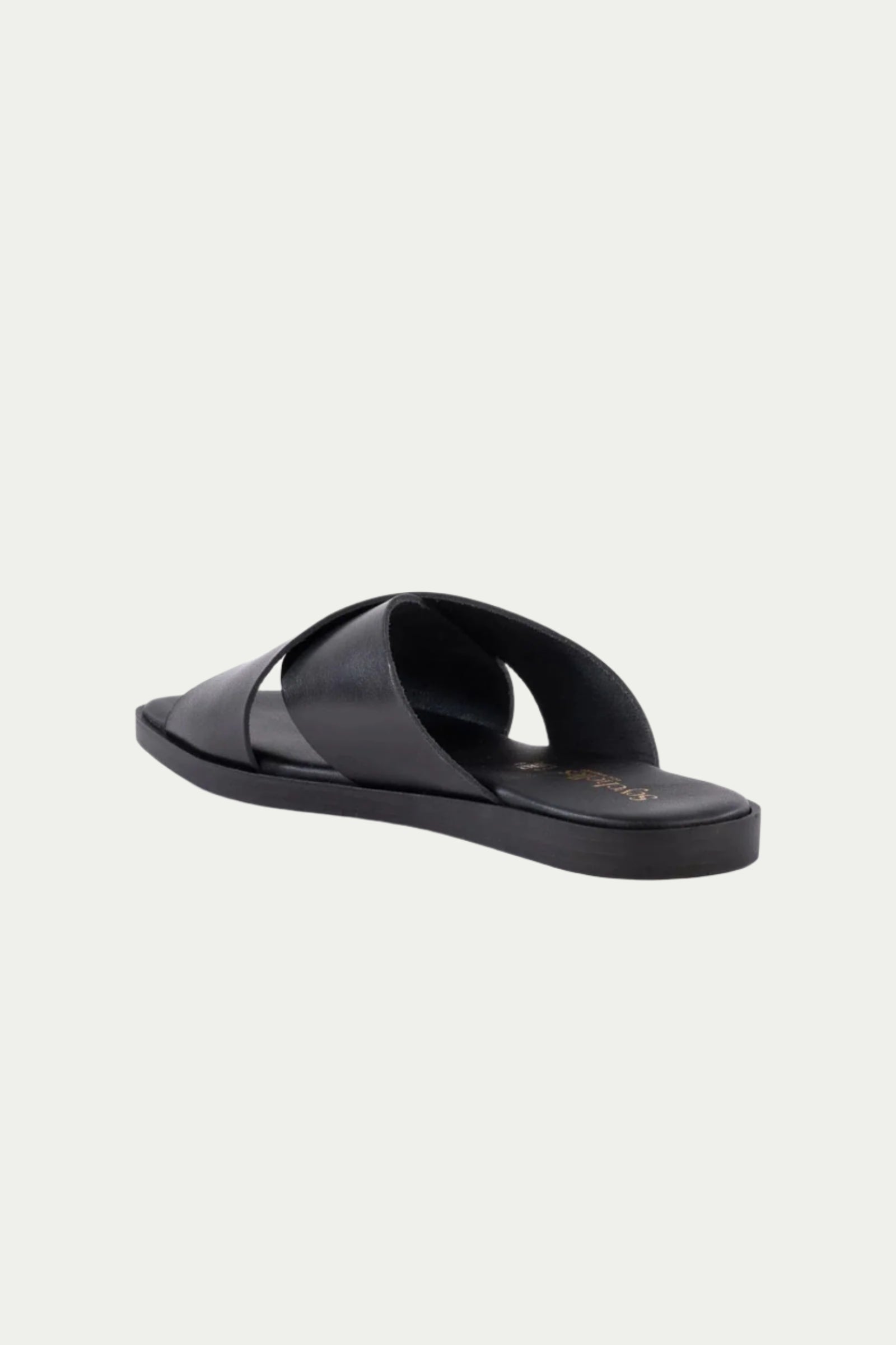 The Chai Sandal - Black Leather features wide crisscross leather straps and a flat sole, shown at an angle from the back and side on a plain white background.