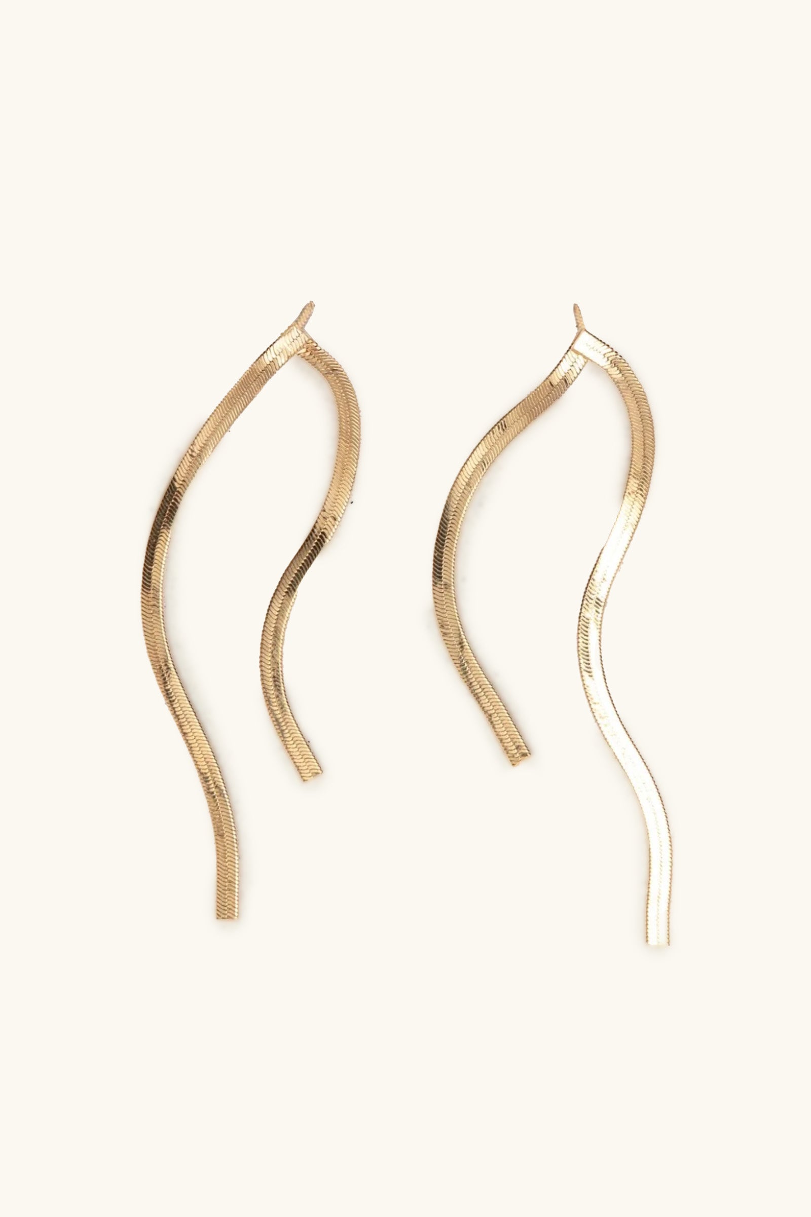 The Lucien Earrings are a gold, wavy, elongated pair with a sleek, minimalist design, displayed on a light beige background.